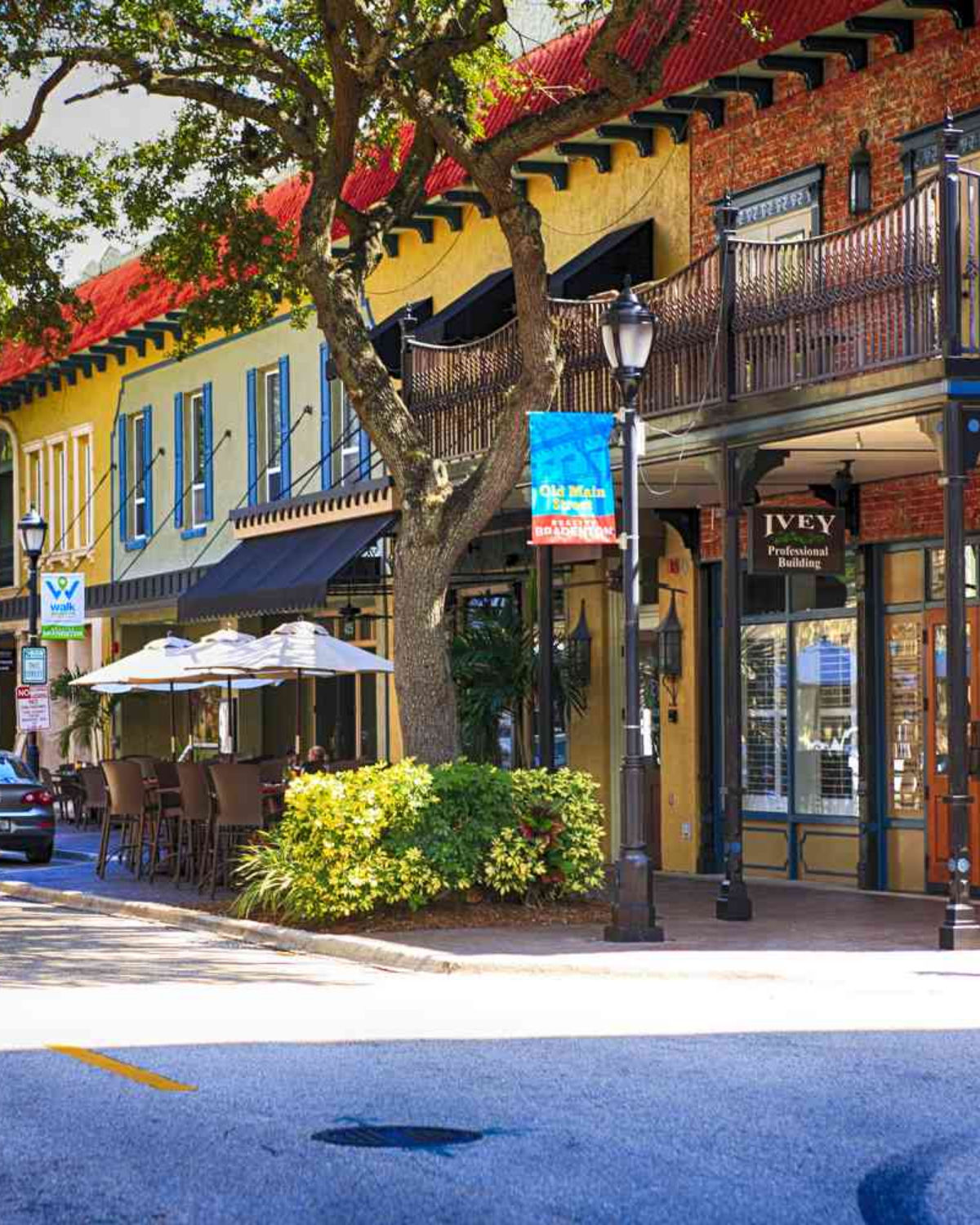 Charming brick-lined streetscape in downtown Bradenton, FL with locally owned shops, outdoor cafe seating, and lush tropical trees