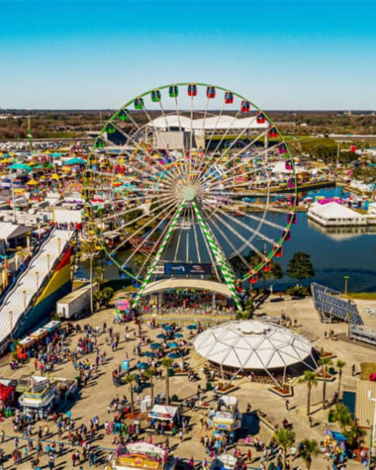 Aerial view of Hillsborough County Fair near Brandon, Florida, showing a  Ferris wheel rising over busy grounds packed with colorful tents, rides, food stands, and crowds