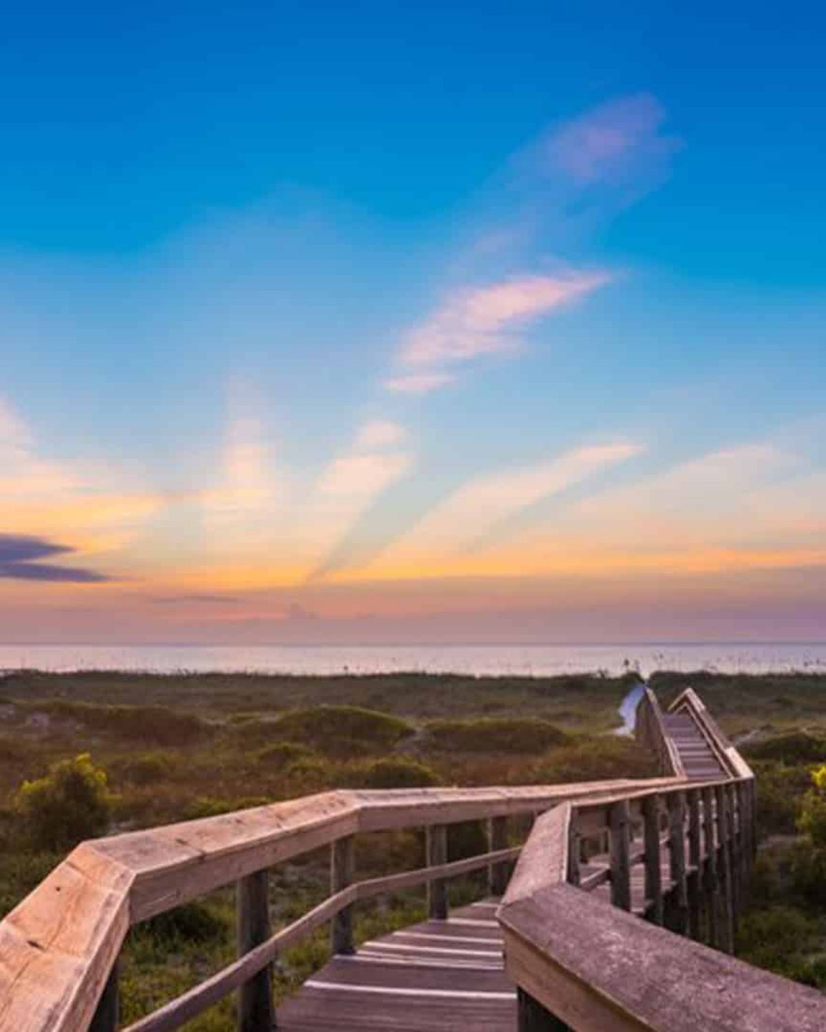 Wooden boardwalk at Fort Clinch State Park in Fernandina Beach, Florida, leading over dunes and sea grass toward the ocean at sunrise.