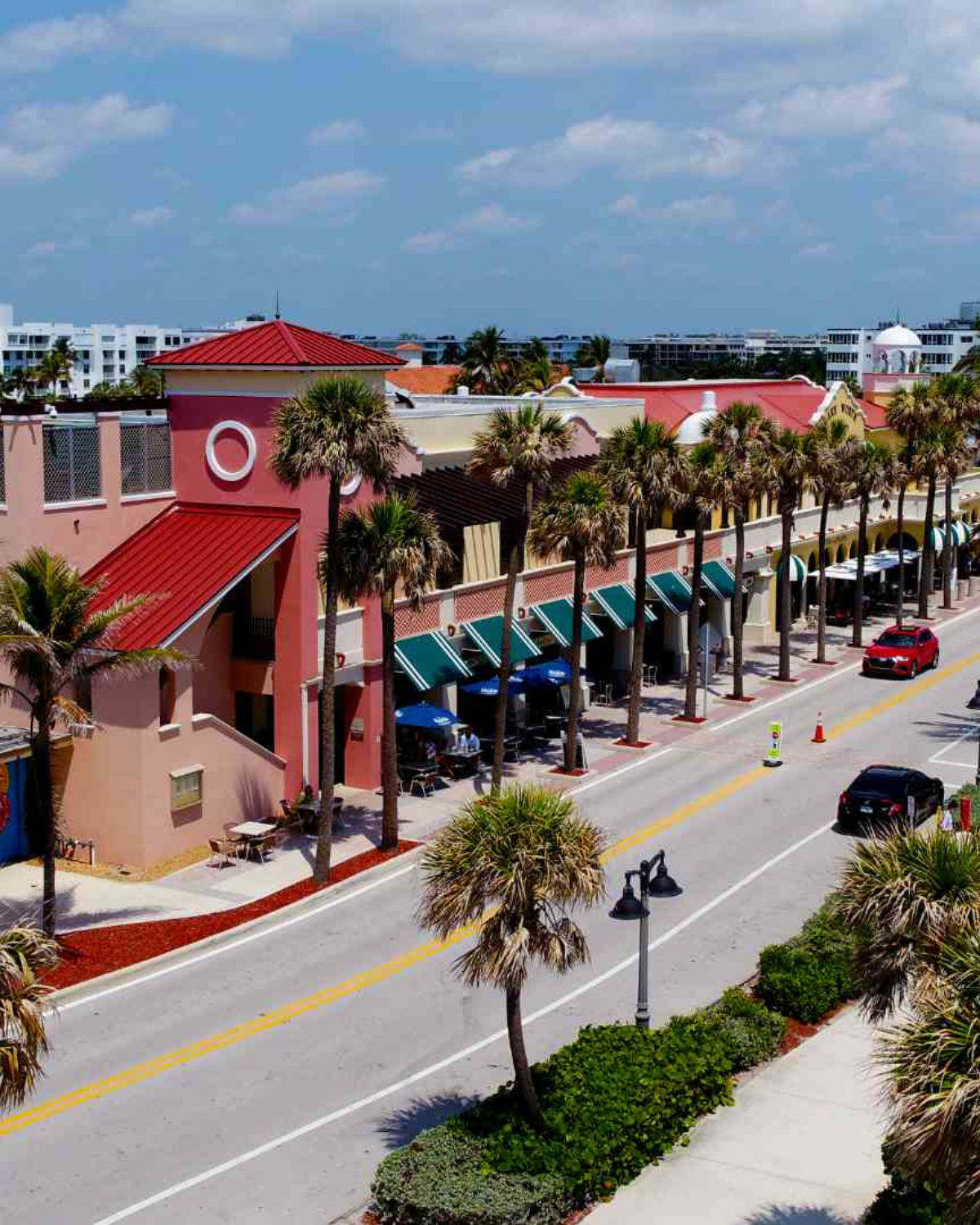 Colorful streetscape of downtown Lake Worth Beach, FL with palm trees, shops, and pedestrians on a sunny day