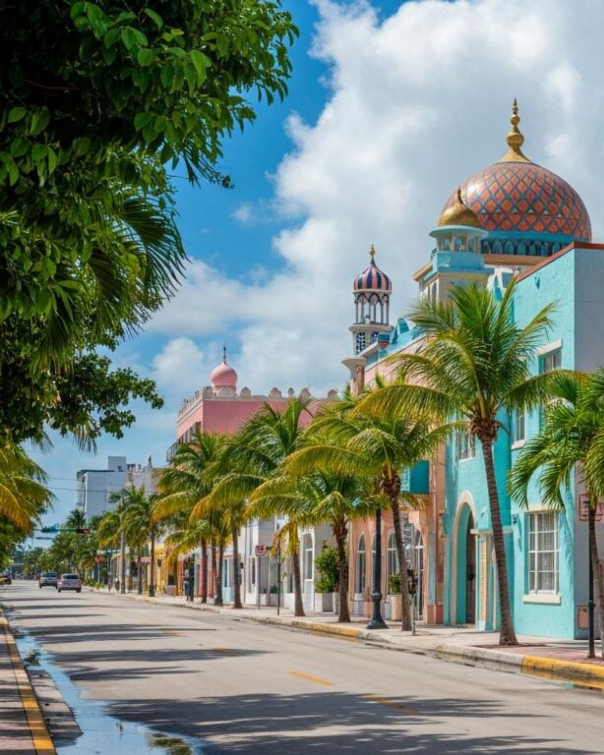 Colorful buildings along a palm-lined street in Opa-locka, Florida, featuring pastel facades, ornate domes, and arched doorways framed by tropical trees.
