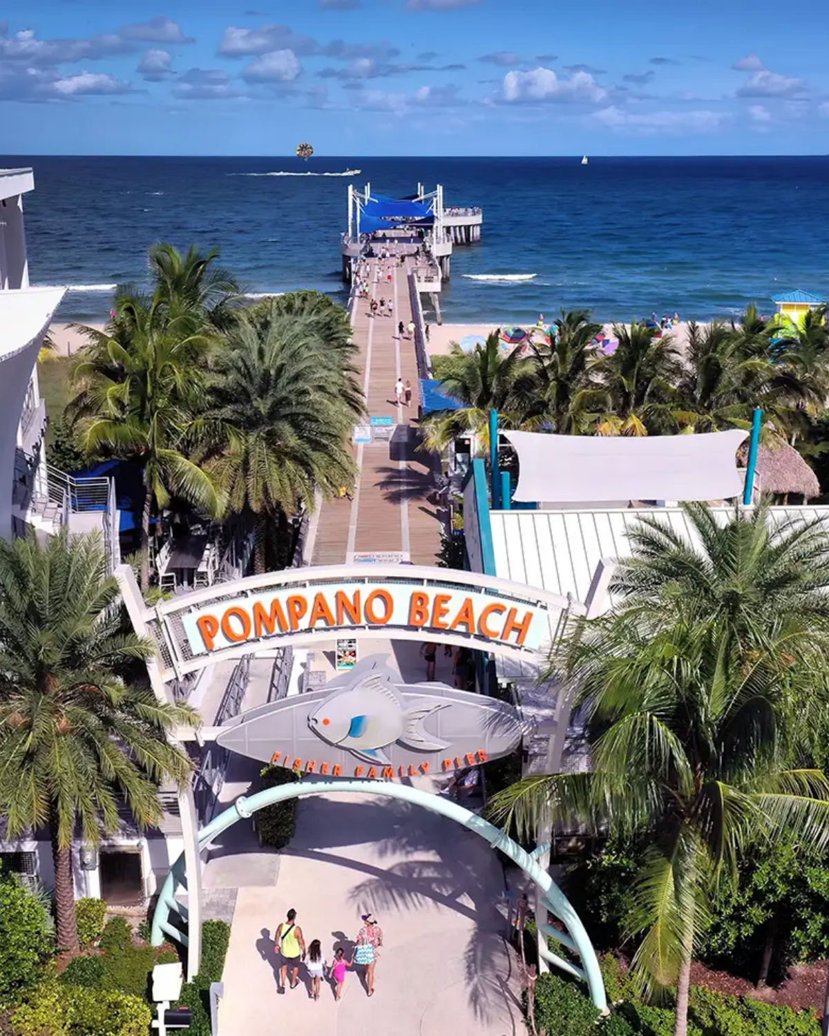 Aerial view of the Pompano Beach sign surrounded by palm trees and colorful beachside buildings in Pompano Beach, FL
