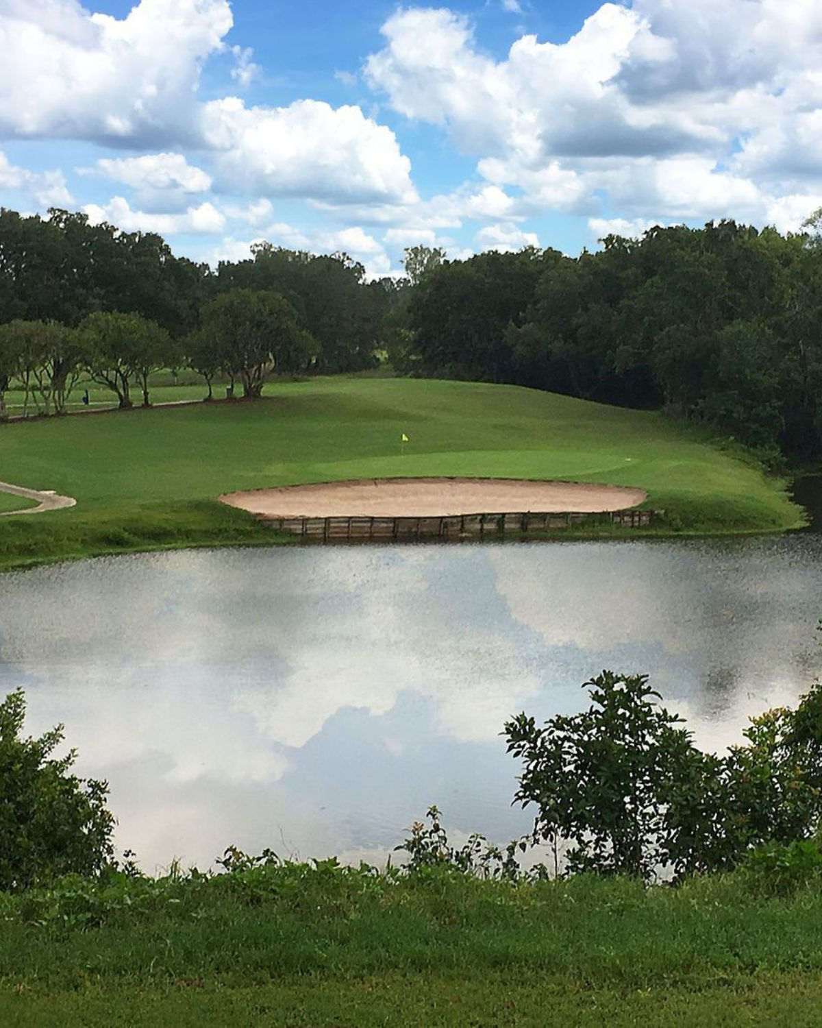 Pond-side view at Diamond Hill Golf Club in Valrico, Florida, looking across the water toward a green with a circular bunker and surrounding fairway framed by trees.