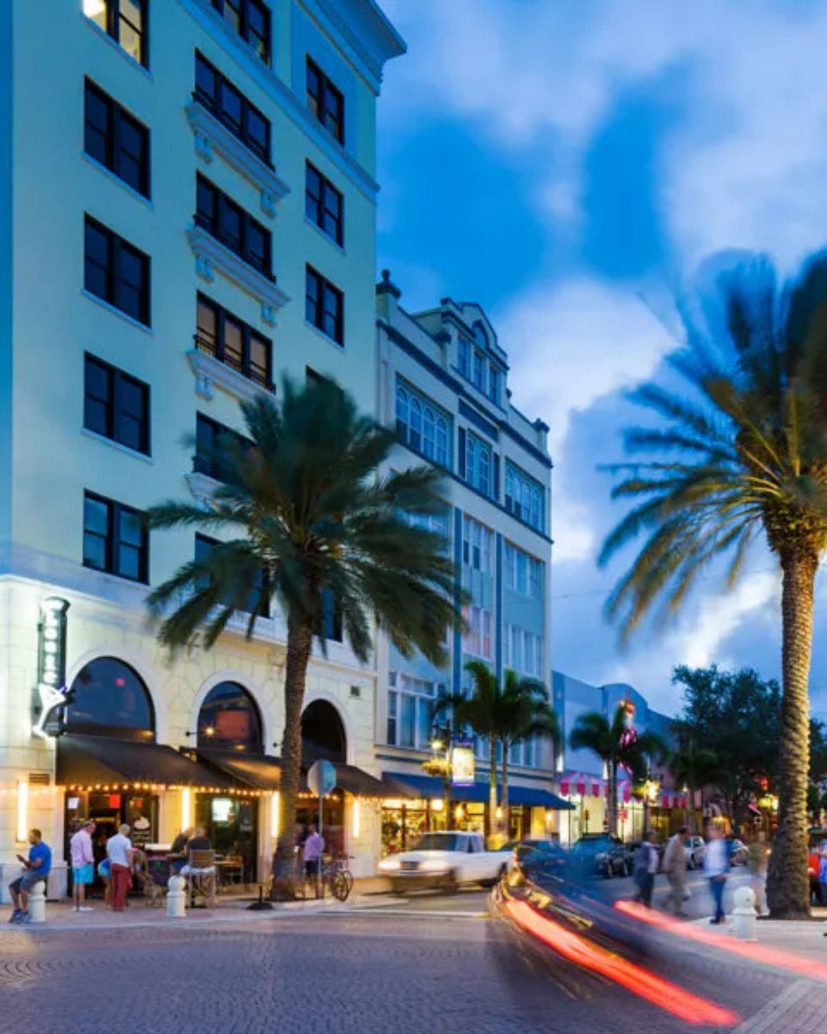 Colorful downtown West Palm Beach street lined with palm trees and blue commercial buildings at dusk