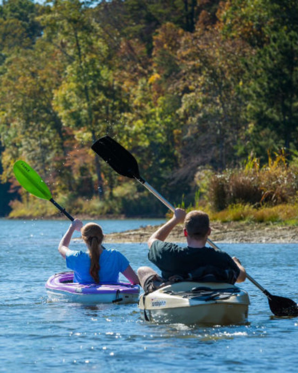 Two people kayaking on the Etowah River in Canton, Georgia, paddling toward a tree-lined bend, with early autumn foliage along the riverbank