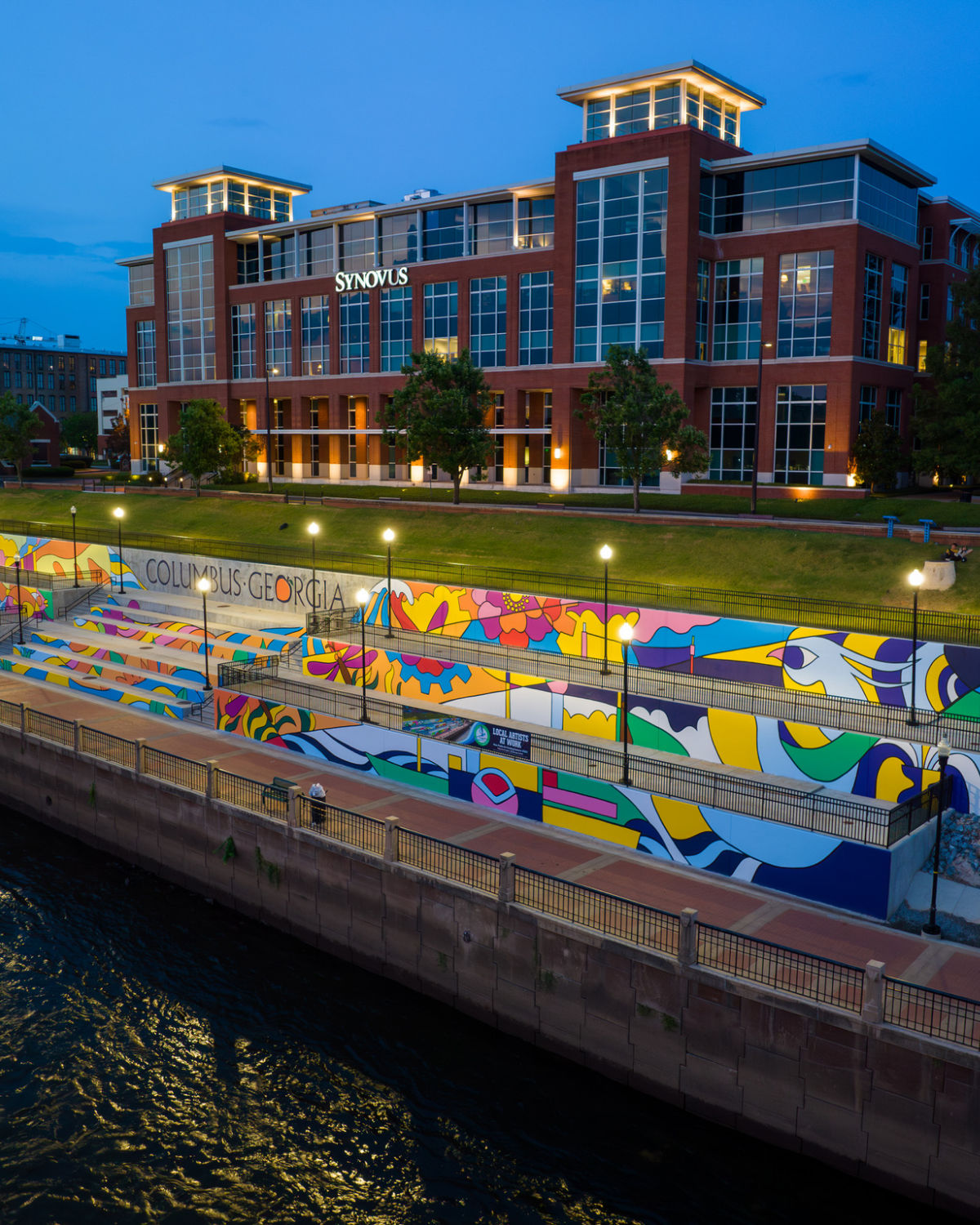 Vibrant colorful murals lining the Chattahoochee Riverwalk at night with illuminated walkways and trees in Columbus, Georgia