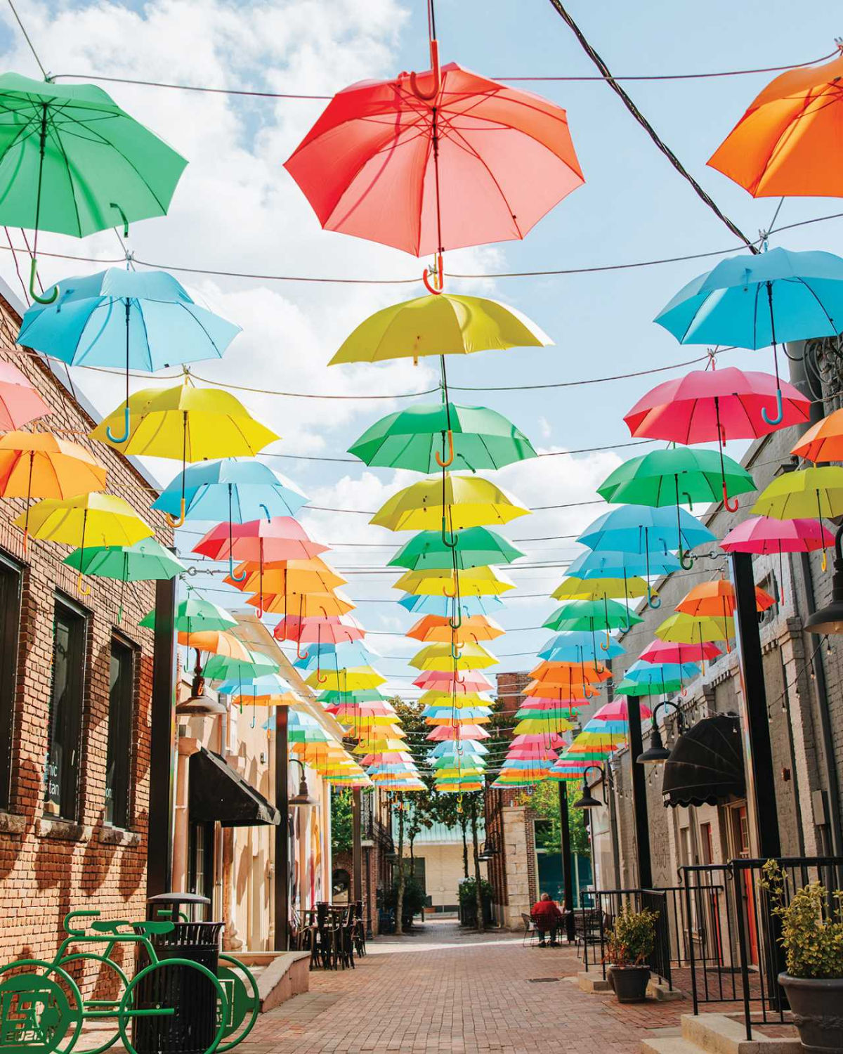 Colorful hanging umbrella art installation above a pedestrian walkway in Olde Town Conyers, Georgia creating a vibrant canopy of red, yellow, blue, and green