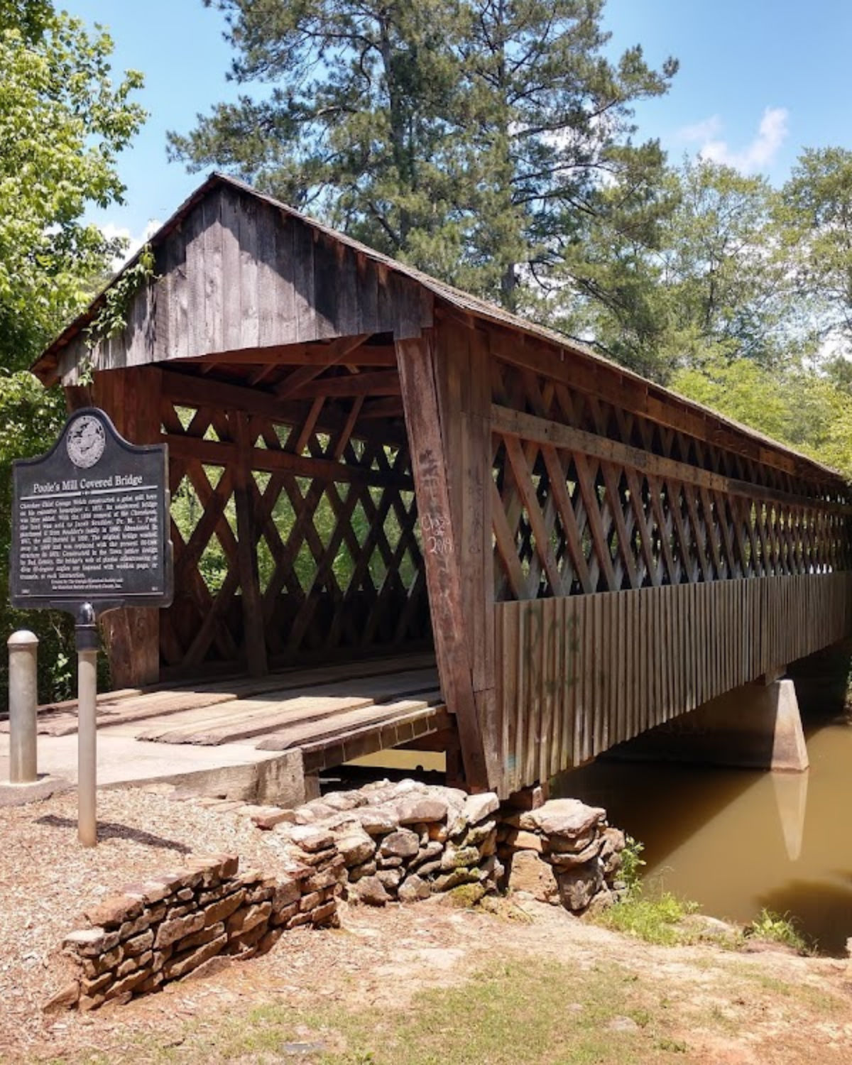 A historic covered bridge with wooden lattice siding surrounded by trees at Poole's Mill Bridge Park in Cumming, Georgia