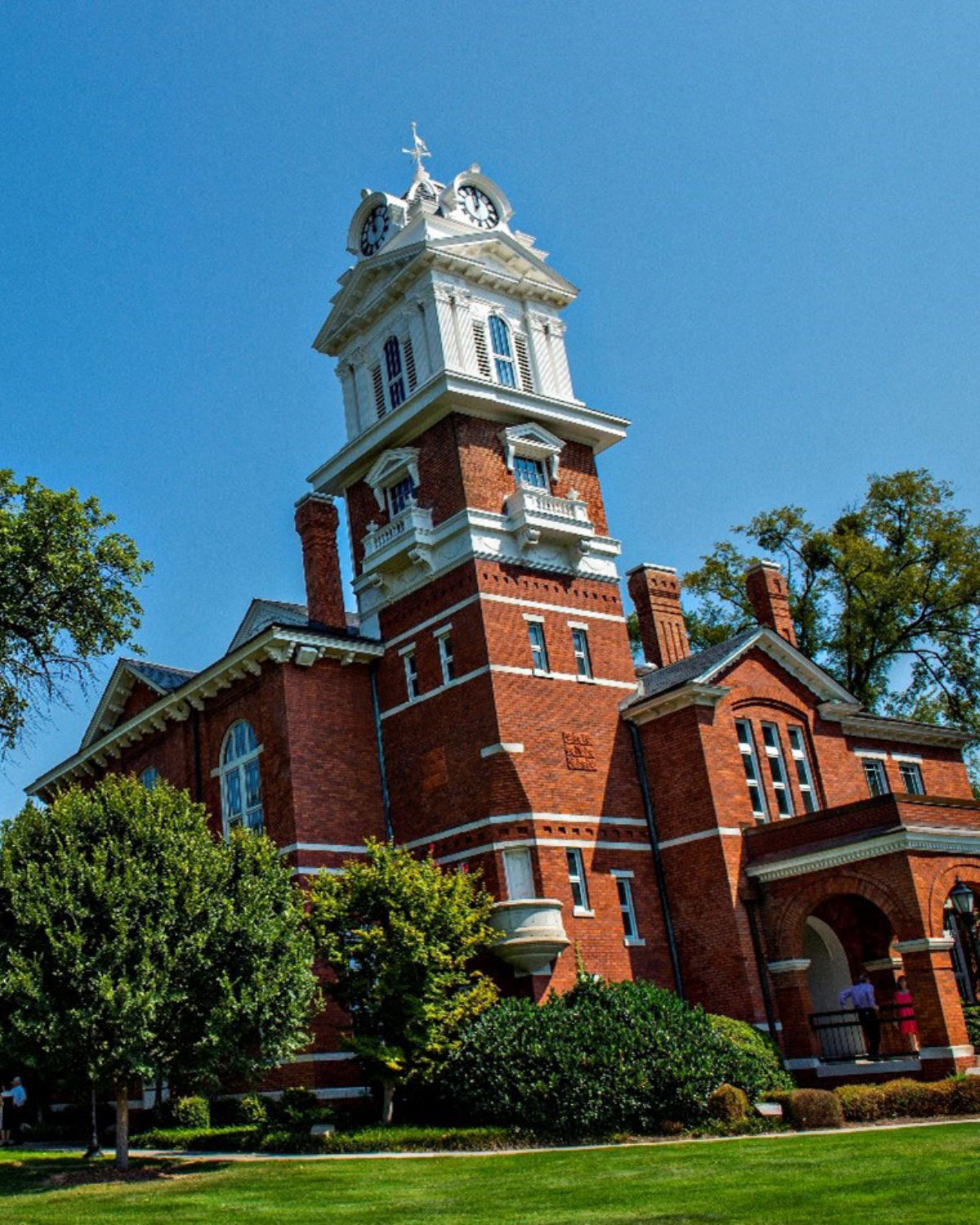 The historic red brick Gwinnett County Courthouse with a white clock tower and steeple surrounded by mature trees in Lawrenceville, Georgia