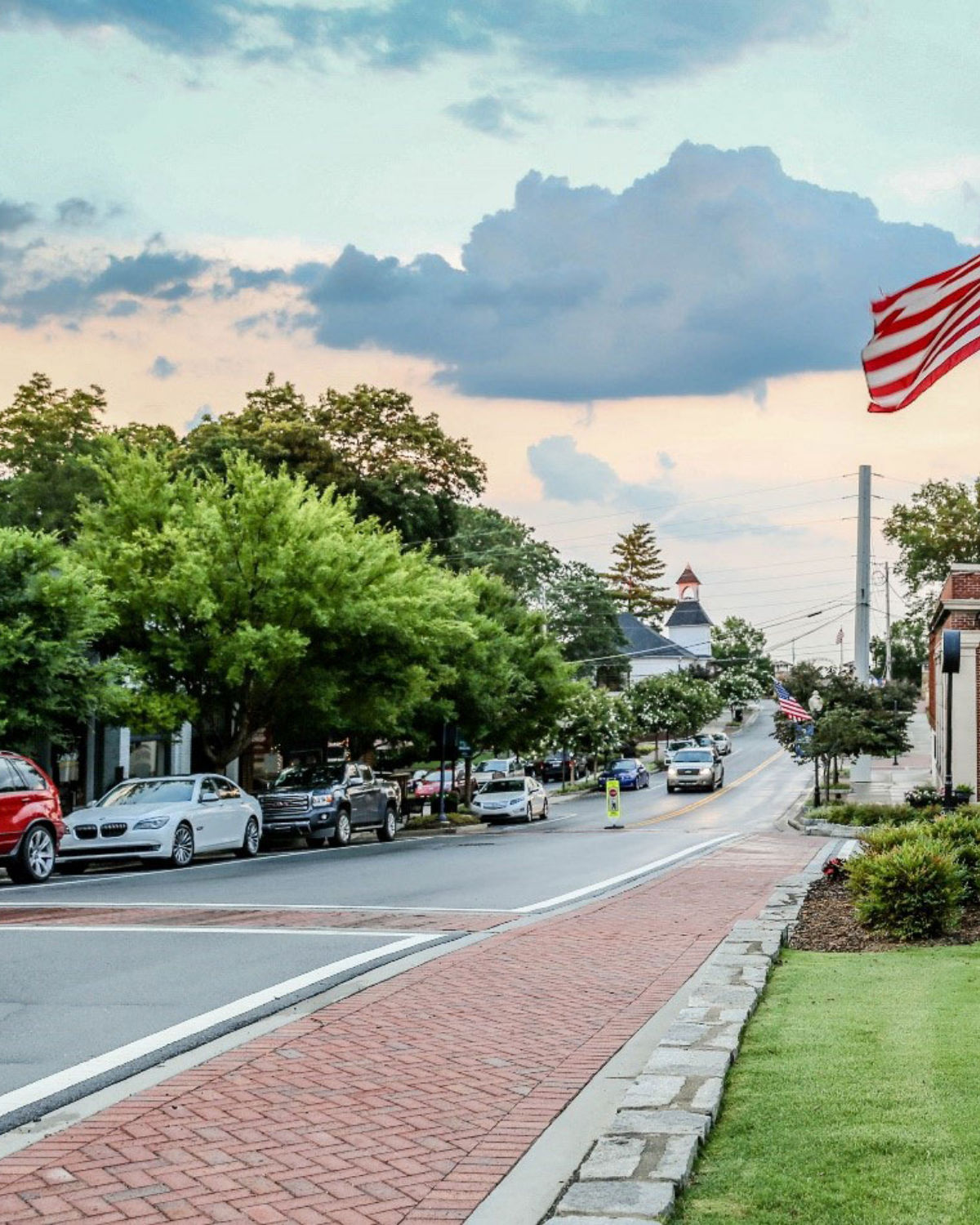 Vibrant outdoor dining scene on a brick-lined street in Historic Downtown Norcross, GA with string lights, restaurant patios, and lush greenery
