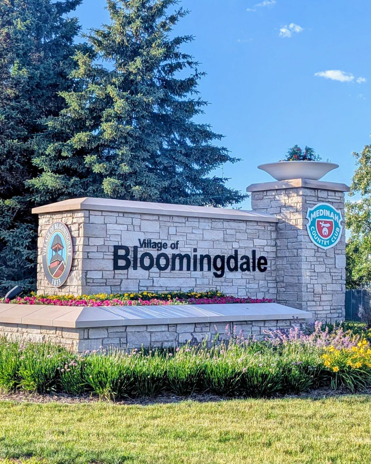 Bloomingdale town plaque surrounded by greenery and tall pines in Bloomingdale, IL