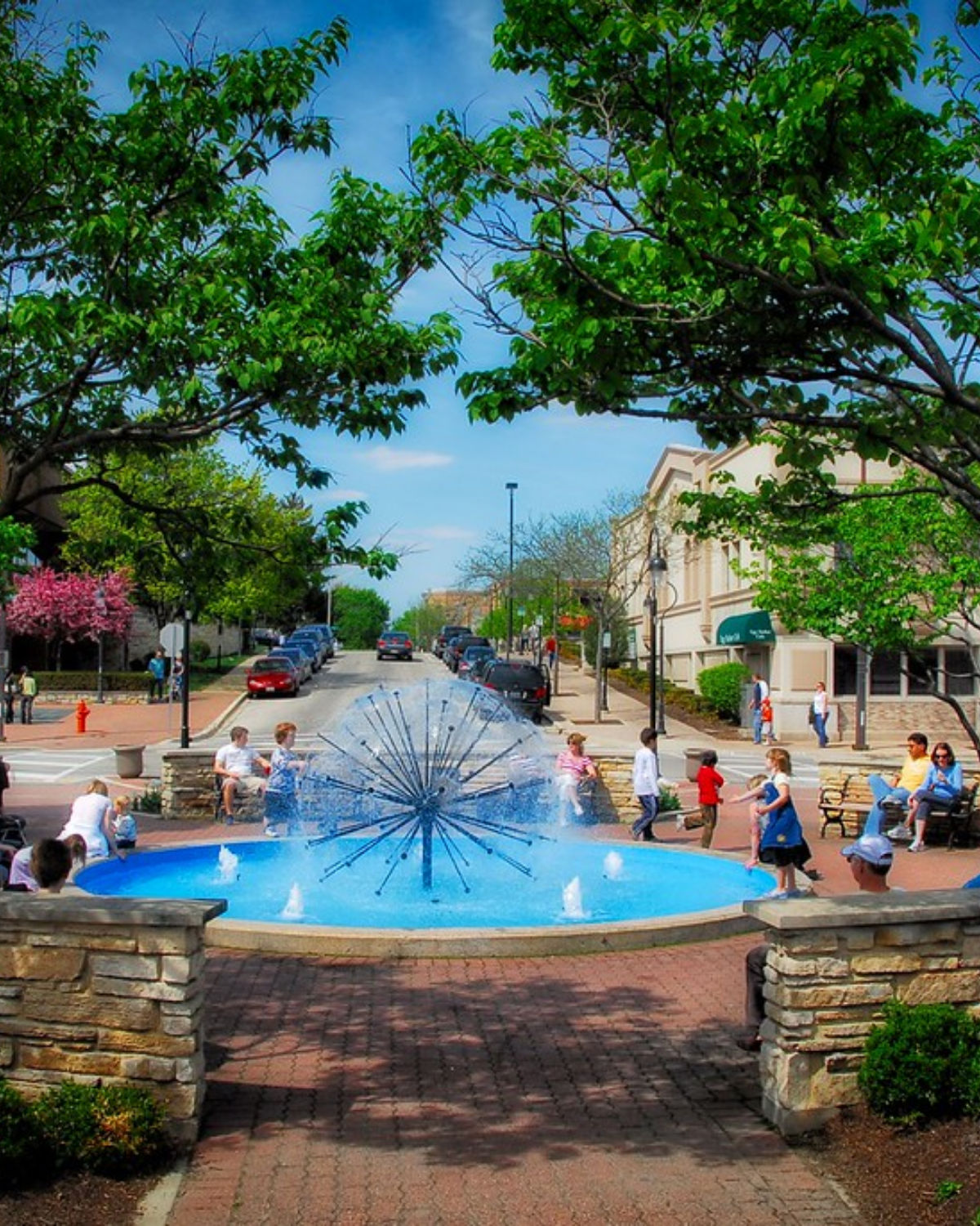 Families enjoying the iconic Dandelion Fountain splash pad along the Naperville Riverwalk on a warm sunny day in Naperville, Illinois