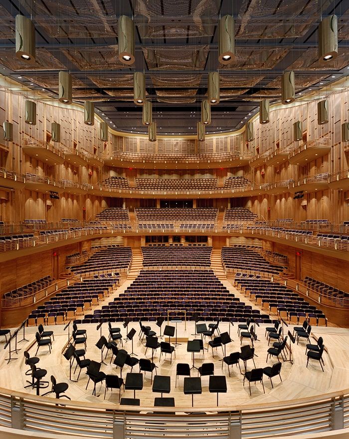 Interior view of a concert hall in Bethesda, Maryland, showcasing a modern performance space with tiered seating, warm wood paneling, suspended acoustic panels, and a stage set with chairs and music stands, reflecting the areaÕs strong arts and cultural scene.