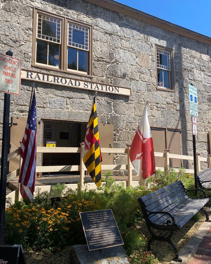 Exterior of the B&O Ellicott City Station Museum in Ellicott City, Maryland, featuring the historic stone railroad station with American and Maryland flags at the entrance.