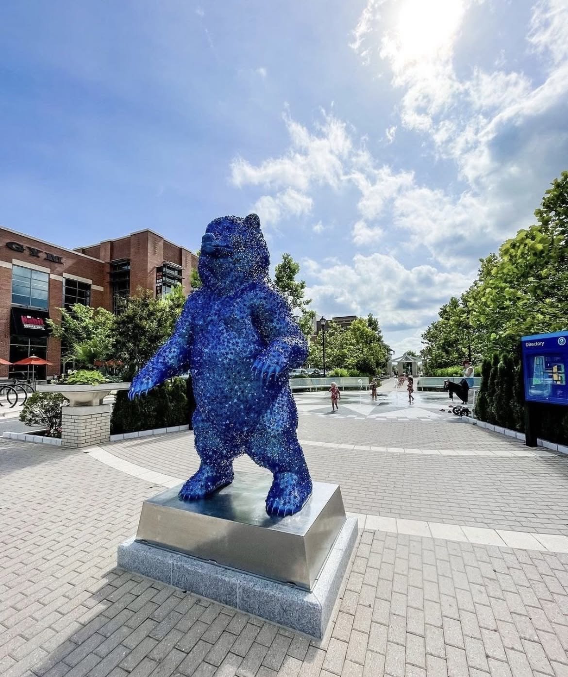 Blue bear sculpture at The Station at Riverdale Park in Riverdale, Maryland, featuring a vibrant public art installation in a modern outdoor plaza with shops, walkways, landscaping, and visitors enjoying the space.
