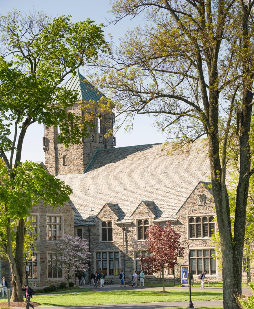 Historic university building in Towson, Maryland, surrounded by tall trees, landscaped grounds, and students walking across campus on a sunny day.