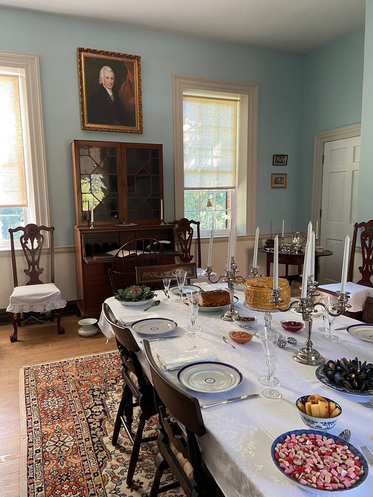 Historic dining room inside the Darnall's Chance House Museum in Upper Marlboro, Maryland, featuring a formally set table with period furnishings, silver candelabras, antique china, wooden furniture, and a portrait displayed above a historic cabinet.