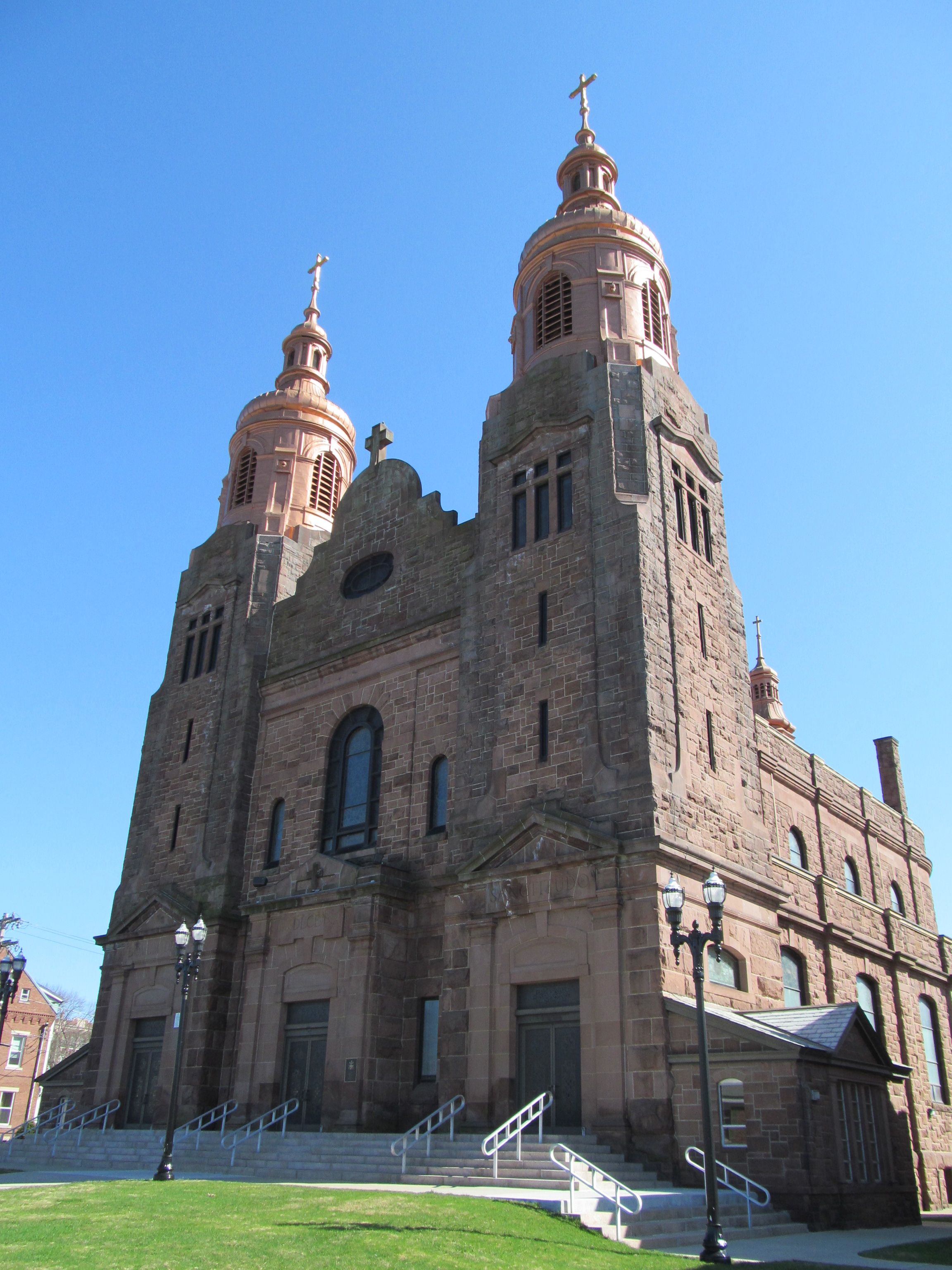 Exterior view of the Basilica of Saint Stanislaus in Chicopee, Massachusetts, featuring its historic stone façade, twin bell towers, and Romanesque architecture under a clear blue sky.