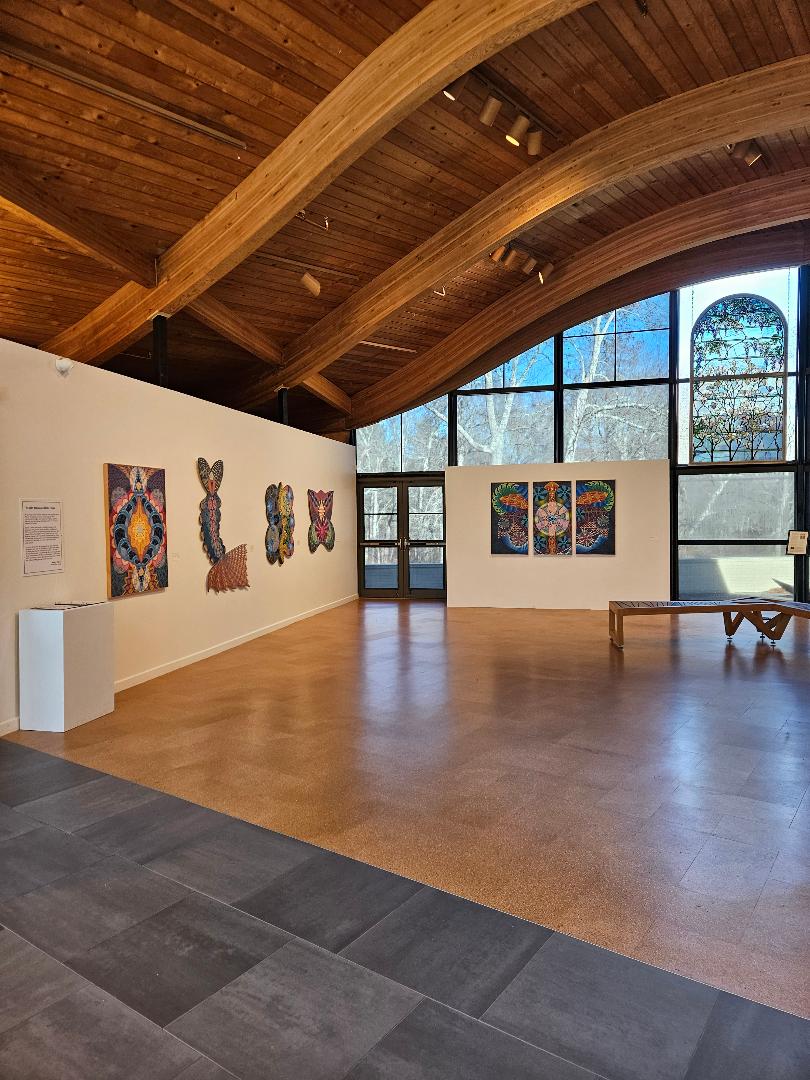 Interior view of The Art Complex Museum in Duxbury, Massachusetts, featuring modern curved architecture surrounded by trees, landscaped greenery, a small reflective pond, and a peaceful wooded setting on a sunny day.