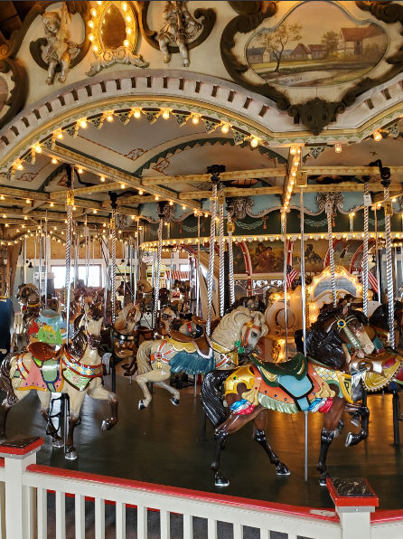Interior view of the historic Paragon Carousel in Hull, Massachusetts, featuring brightly painted carousel horses, vintage decorative artwork, glowing string lights, and the classic seaside amusement atmosphere inside the carousel pavilion.
