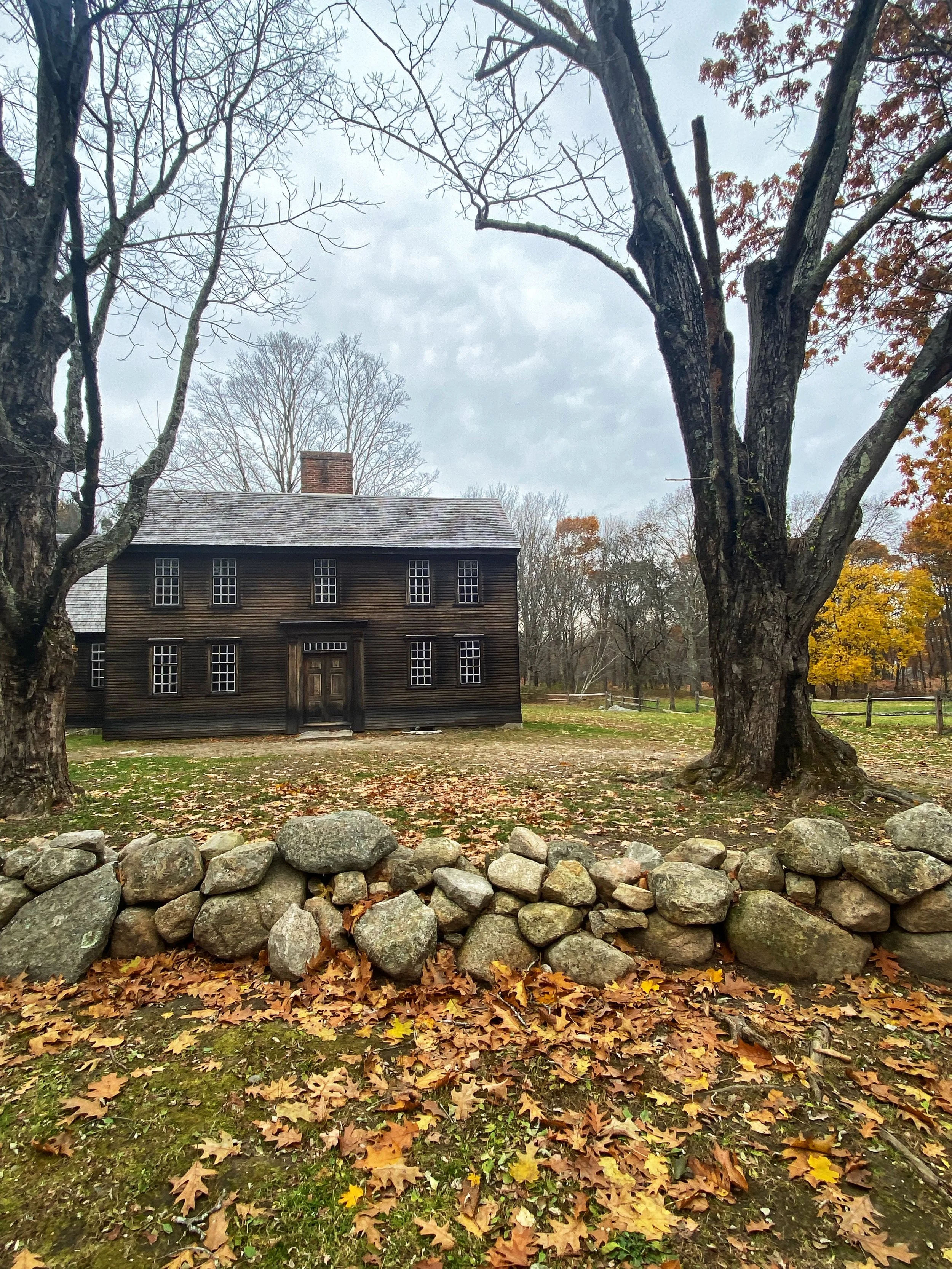 Exterior view of the historic Buckman Tavern in Lexington, Massachusetts, featuring the preserved colonial-era building, stone wall, and autumn landscape that reflect the town’s Revolutionary War heritage.