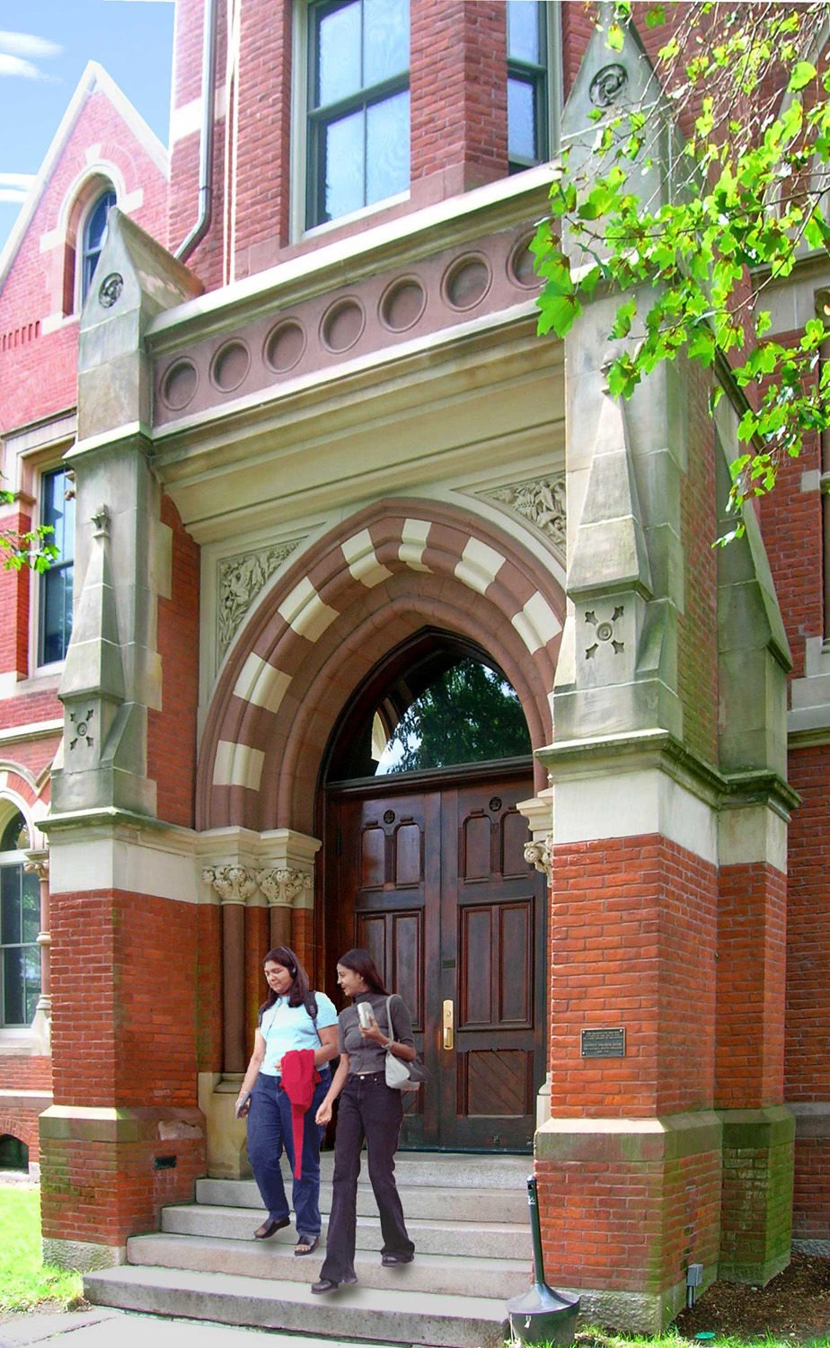 The entrance to a historic academic building at Smith College in Northampton, Massachusetts, with students walking down the front steps beneath Gothic-style stone arches and mature shade trees.