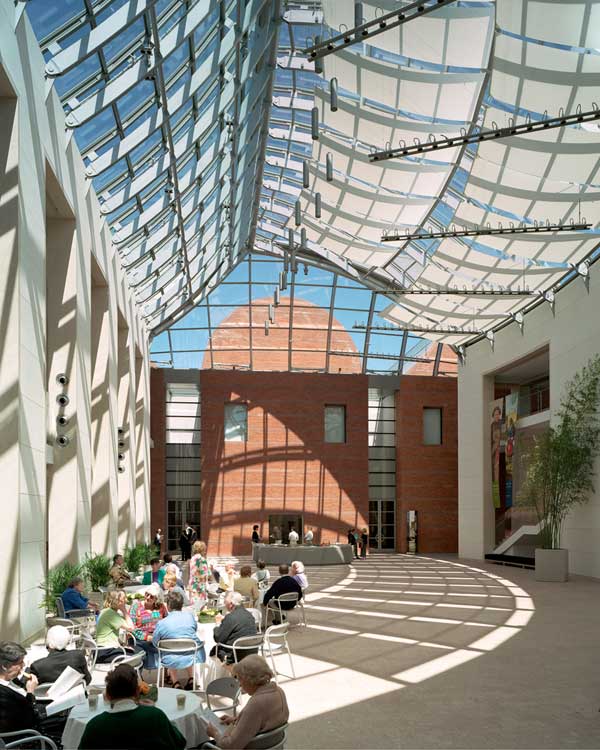 The bright glass atrium inside the Peabody Essex Museum in Peabody, Massachusetts, featuring modern architecture, natural light, indoor seating, and visitors gathered in the spacious lobby.