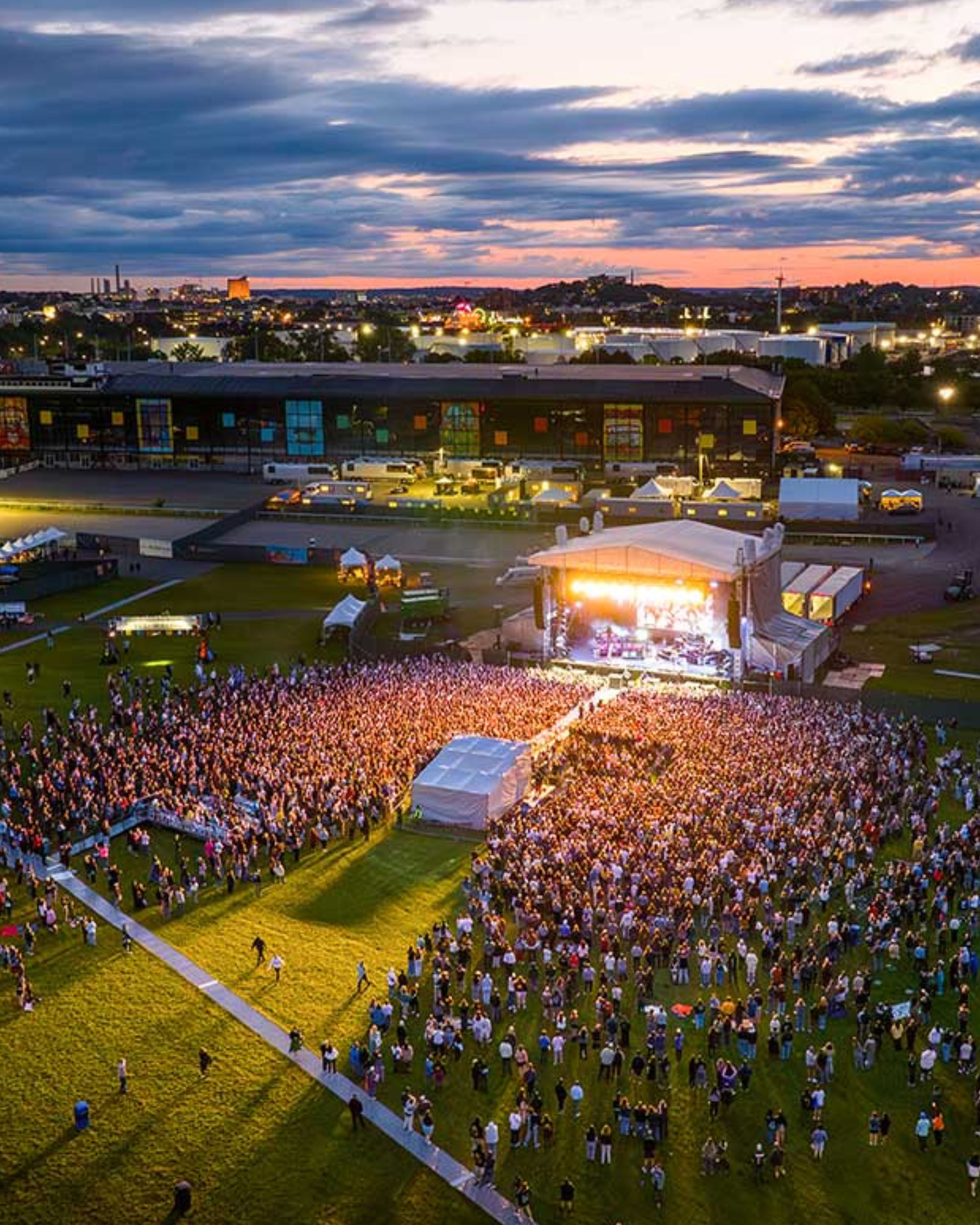 A lively outdoor concert at Suffolk Downs in Revere, Massachusetts, draws a large crowd at sunset, highlighting the city’s vibrant community events, entertainment scene, and energetic coastal atmosphere.