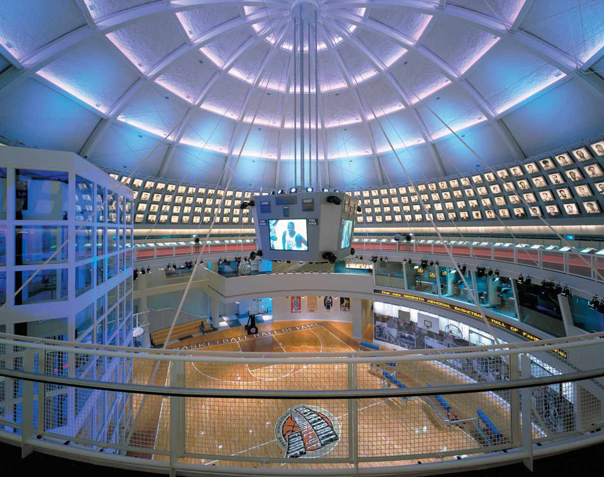 An interior view of the Naismith Memorial Basketball Hall of Fame in Springfield, Massachusetts, featuring a domed ceiling lined with portraits of basketball legends, a central suspended display, and a full basketball court exhibit below.