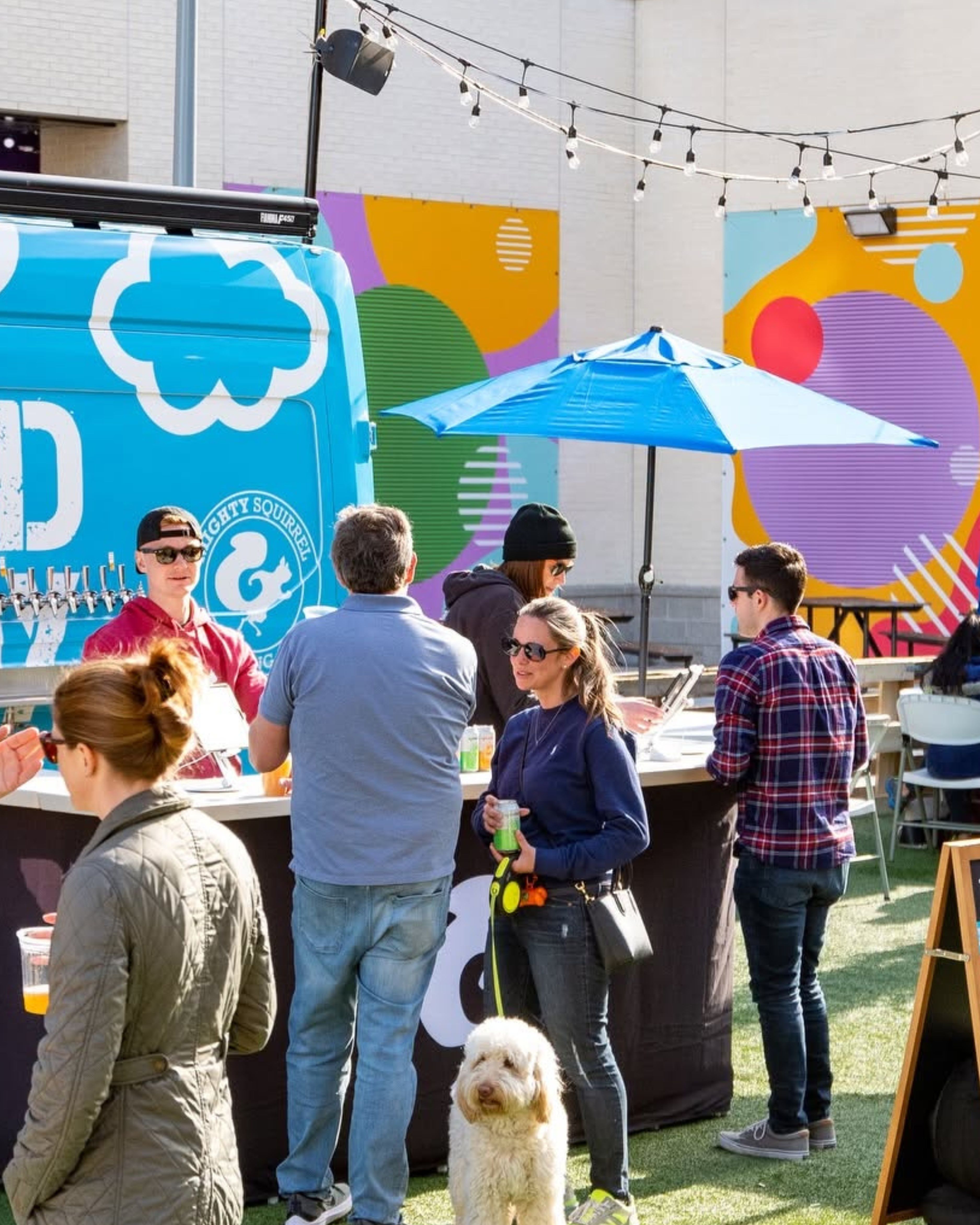 Visitors gather at Mighty Squirrel Brewing Co.'s outdoor beer garden in Waltham, Massachusetts, enjoying craft beer, food, and a pet-friendly atmosphere beneath string lights.