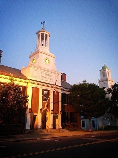 Historic Westborough Town Hall in Westborough, MA at sunset, featuring a classic clock tower, brick facade, and warm evening lighting along a quiet street