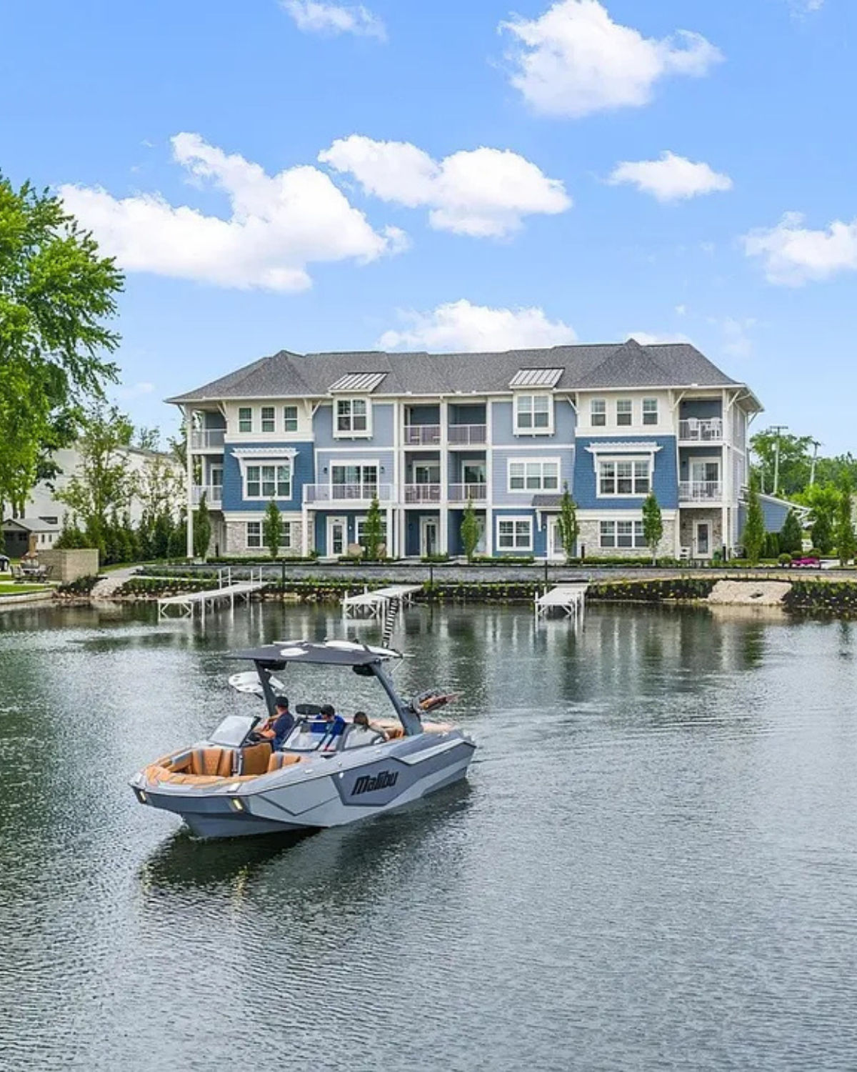 Lakeside in Lake Orion, Michigan, showing a gray speedboat in calm water in front of an apartment building with balconies and boat docks