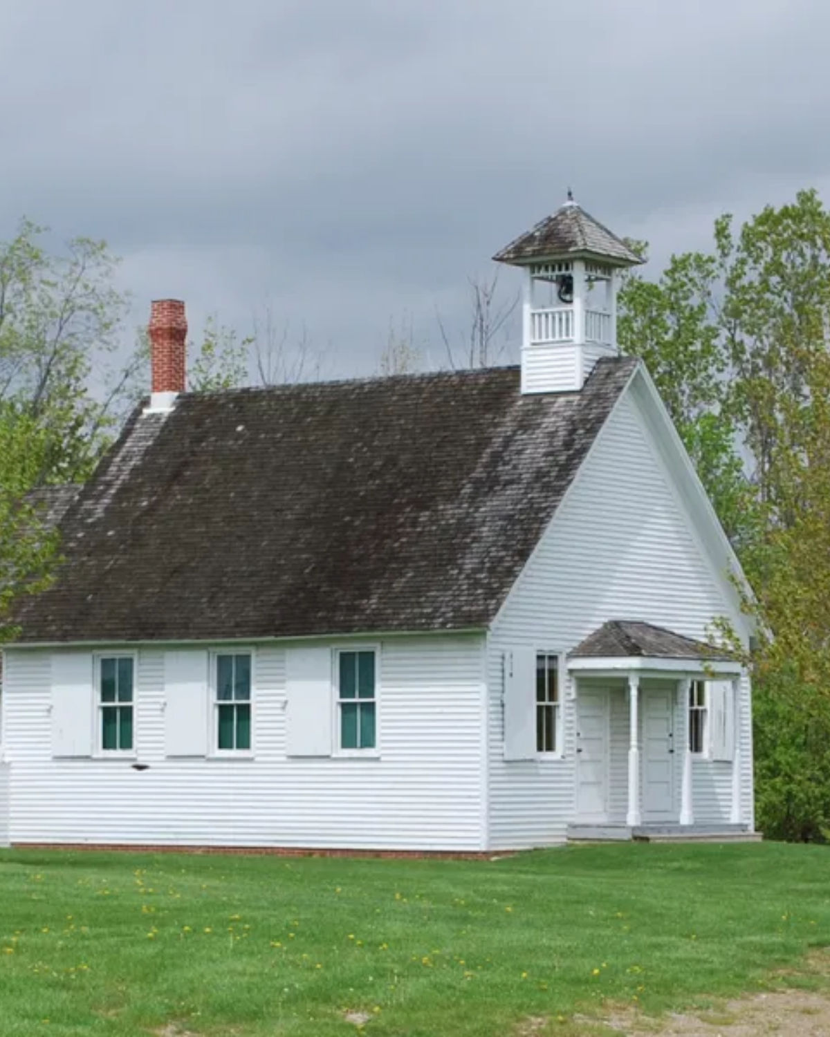 A historic white clapboard one-room schoolhouse with a small bell tower at Greenmead Historical Park in Livonia, Michigan