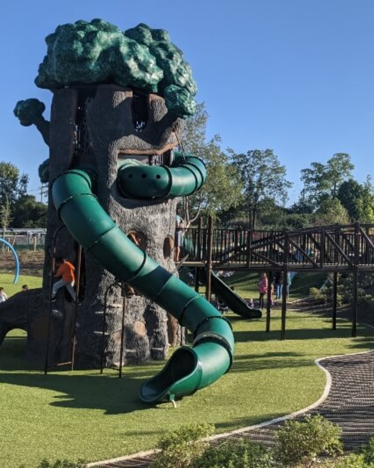 A family enjoying a modern nature-themed playground with rope bridges and wooden climbing structures at Innovation Hills in Rochester Hills, Michigan