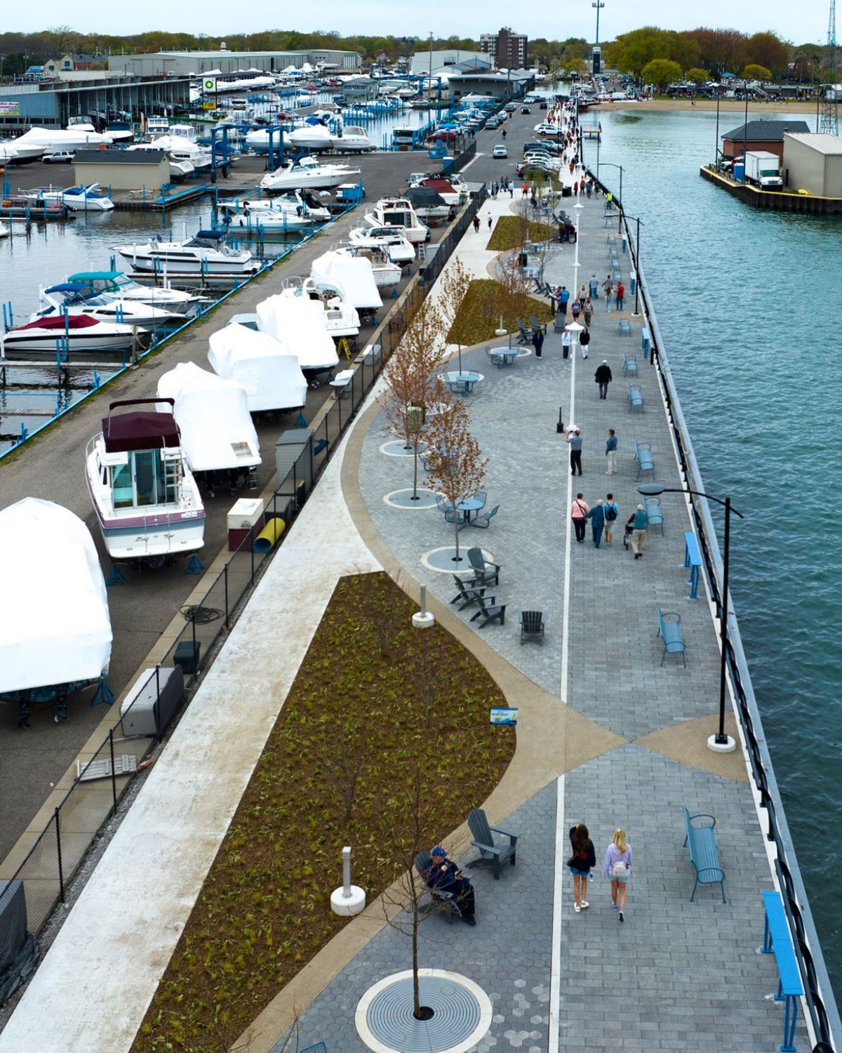 Aerial view of Blossom Heath Pier in Saint Clair Shores, Michigan, showing a long waterfront promenade lined with benches, trees, and walking paths on the water of Lake St. Clair, with marinas full of docked boats
