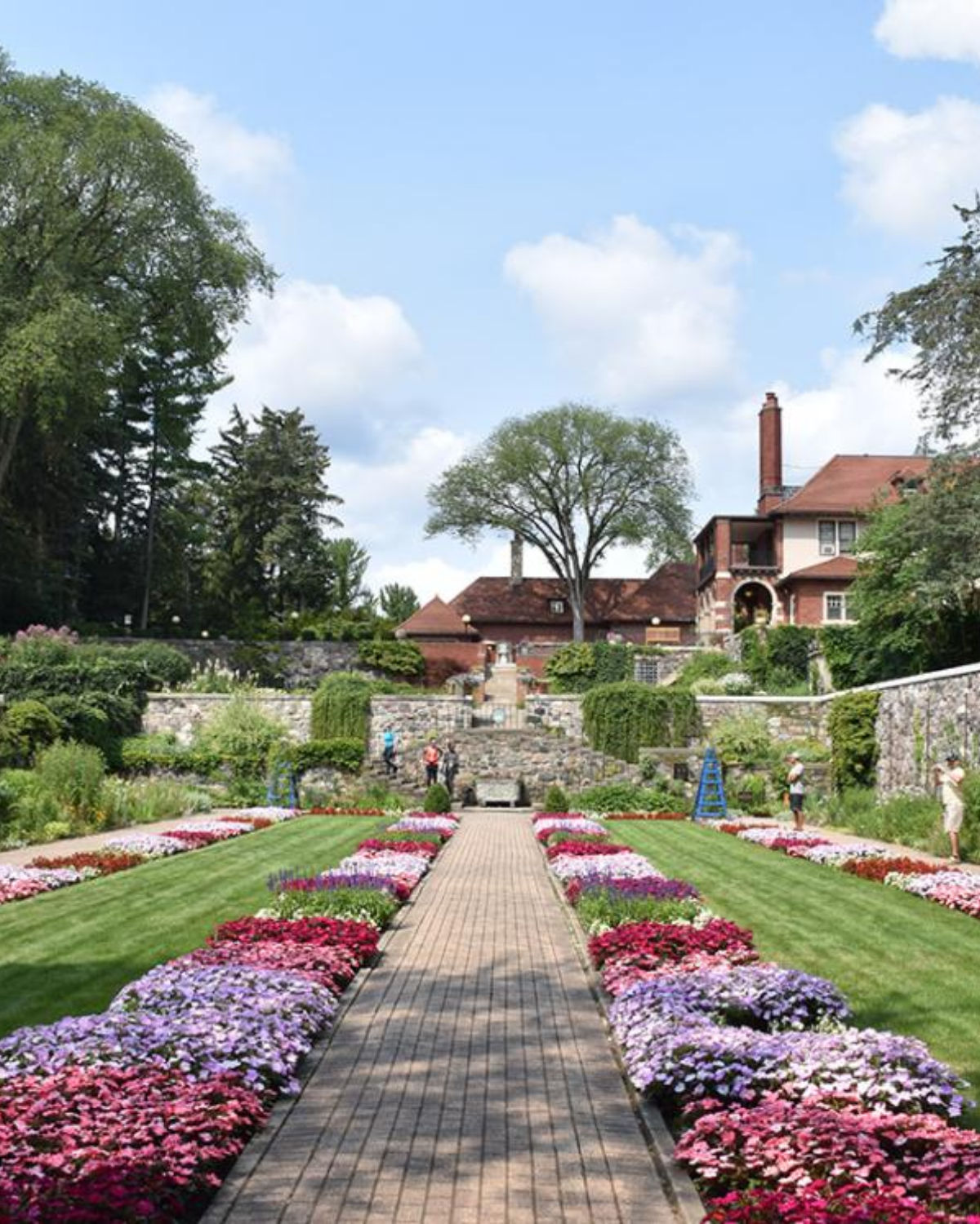 Elegant formal garden with colorful flower beds, manicured hedges, and a grand historic manor at Cranbrook House and Gardens near Troy, Michigan