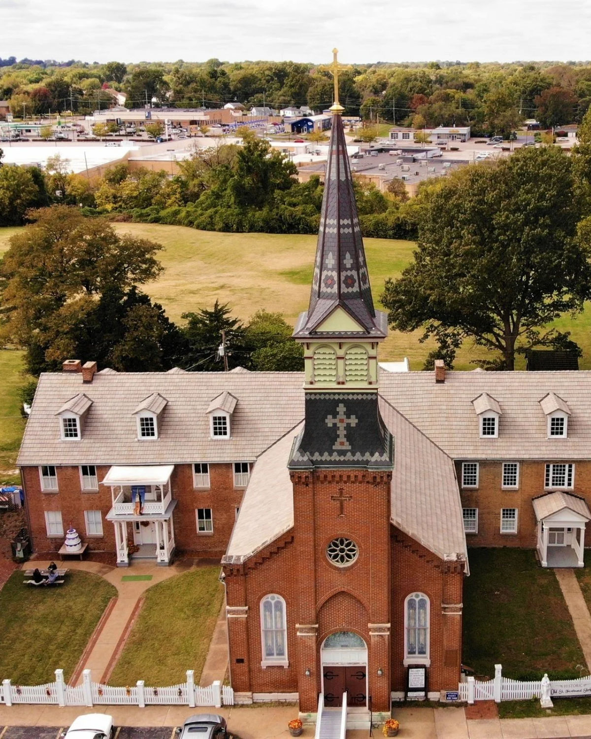 Aerial view of a historic brick church with a tall steeple surrounded by mature trees in Old Town Florissant, Missouri