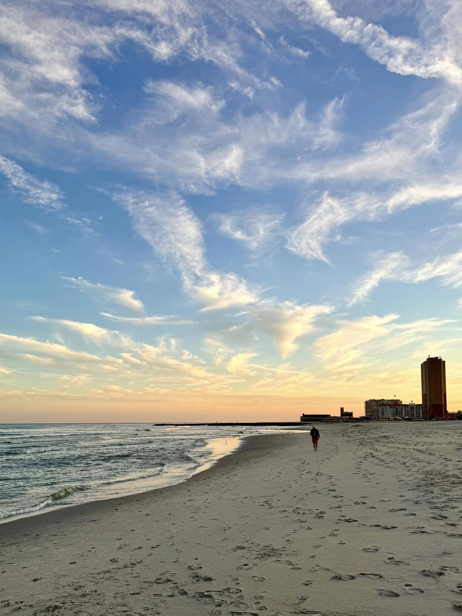 Peaceful sandy beach and Atlantic Ocean shoreline in Allenhurst, New Jersey, with gentle waves and a colorful sunset beneath wispy clouds.