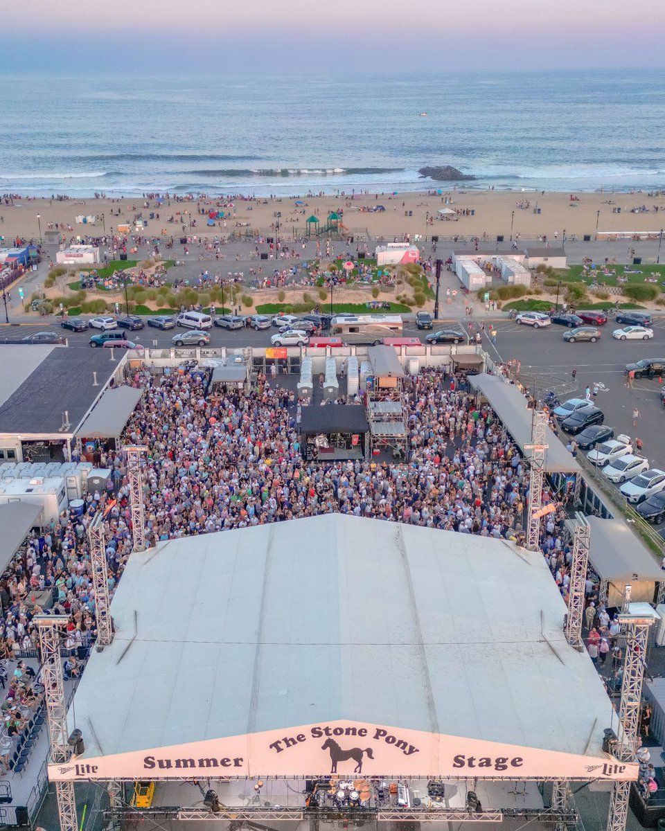 Aerial view of The Stone Pony Summer Stage in Asbury Park, NJ featuring a packed outdoor concert crowd set against the beachfront and ocean backdrop