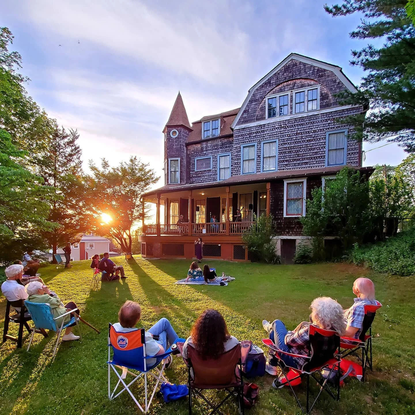 Historic Strauss Mansion Museum in Atlantic Highlands, New Jersey, with visitors relaxing on the lawn during an outdoor community gathering at sunset.