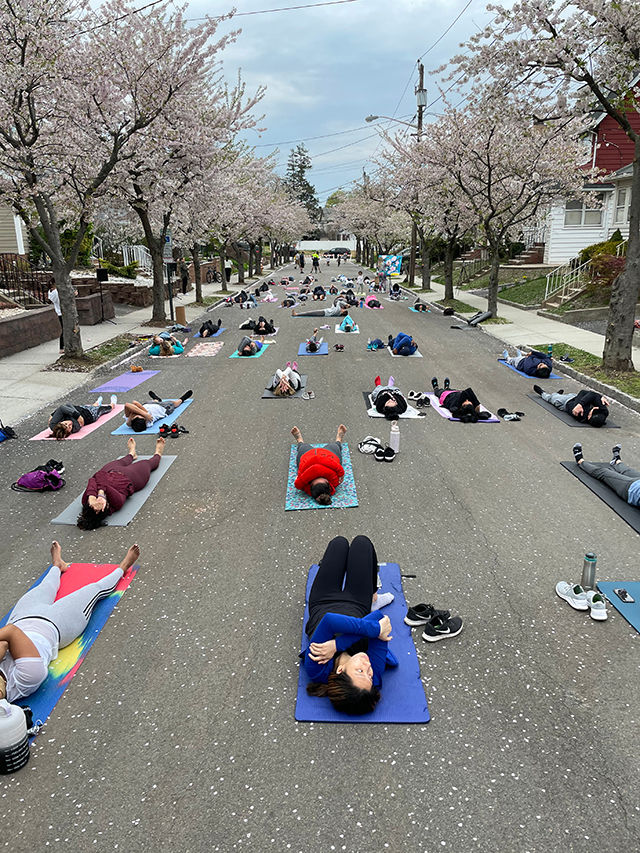 Residents participate in an outdoor community yoga class beneath blooming cherry blossom trees along a neighborhood street in Belleville, New Jersey.
