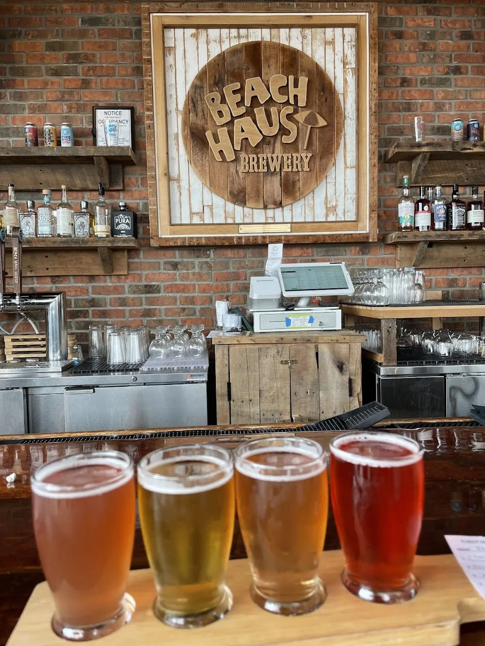 Craft beer flight served at Beach Haus Brewery in Belmar, New Jersey, with the brewery's wooden Beach Haus sign displayed behind the bar.