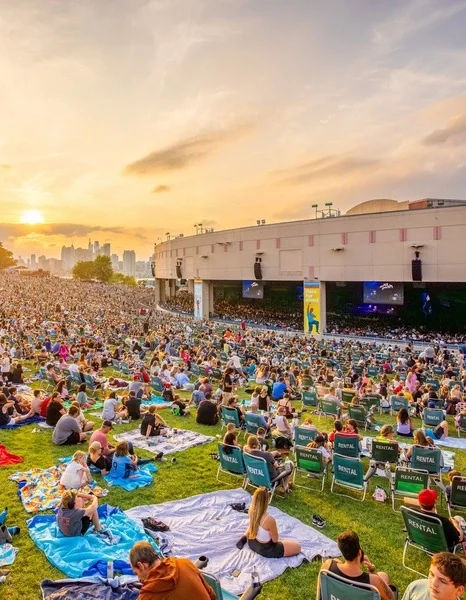 Crowds gather on the lawn outside the Freedom Mortgage Pavilion in Camden, New Jersey, enjoying an outdoor concert with views of the Philadelphia skyline.