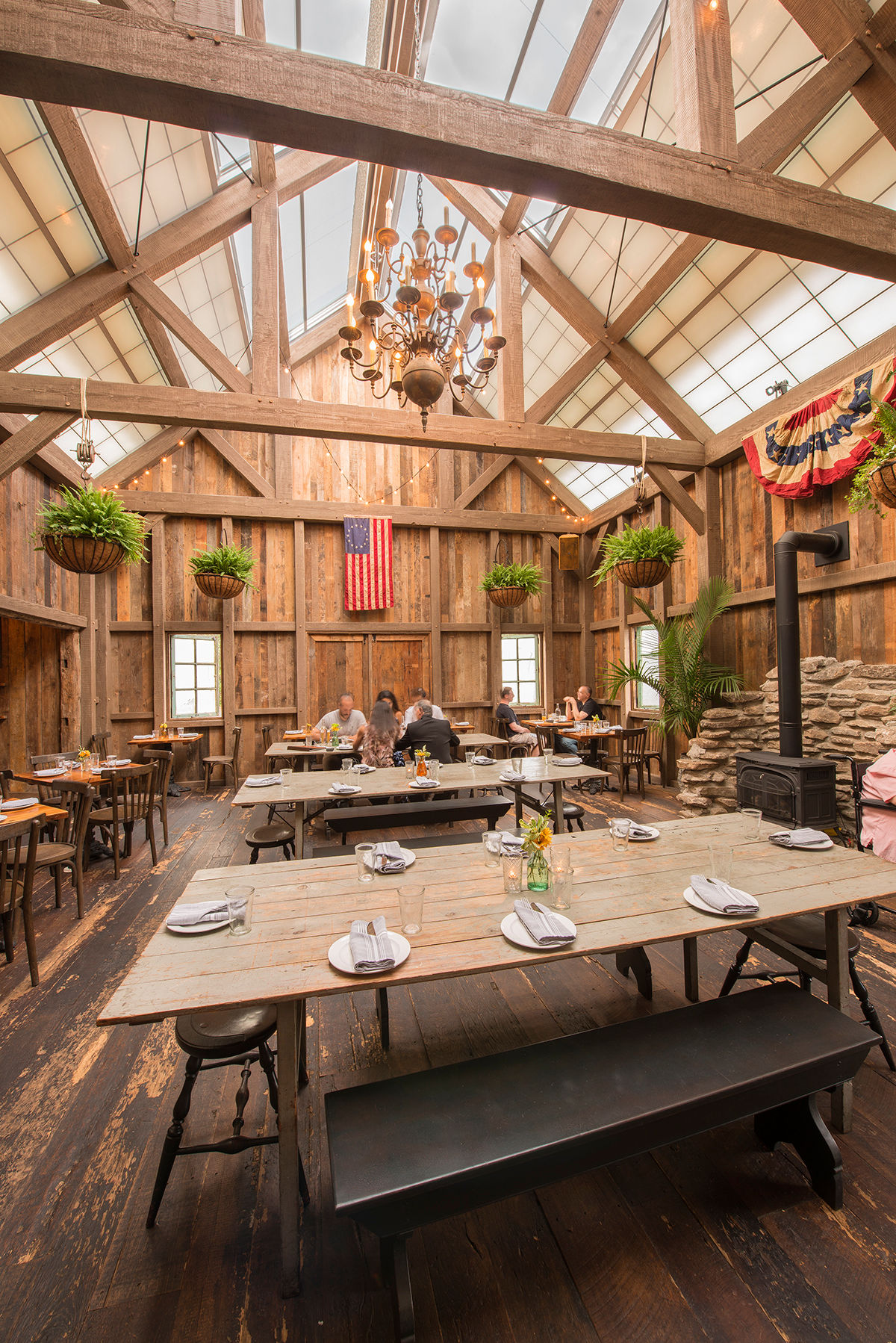 Interior of Barrow House in Clifton, New Jersey, featuring a rustic timber-frame dining room with communal tables, exposed wood beams, and historic barn-inspired architecture.