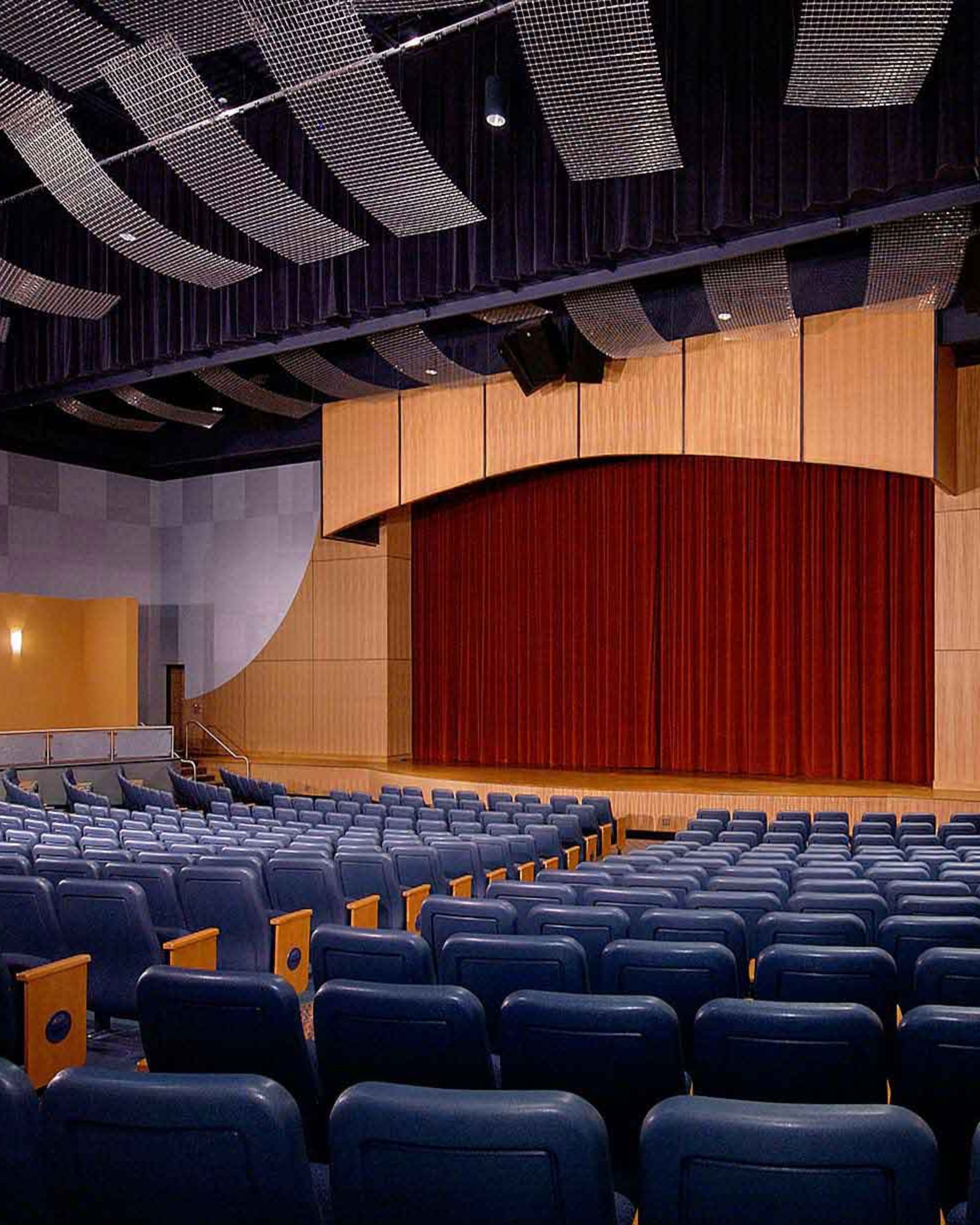 Spacious auditorium in Deal, New Jersey, featuring rows of blue theater seats, a large performance stage, red curtain, and modern wood-paneled interior.