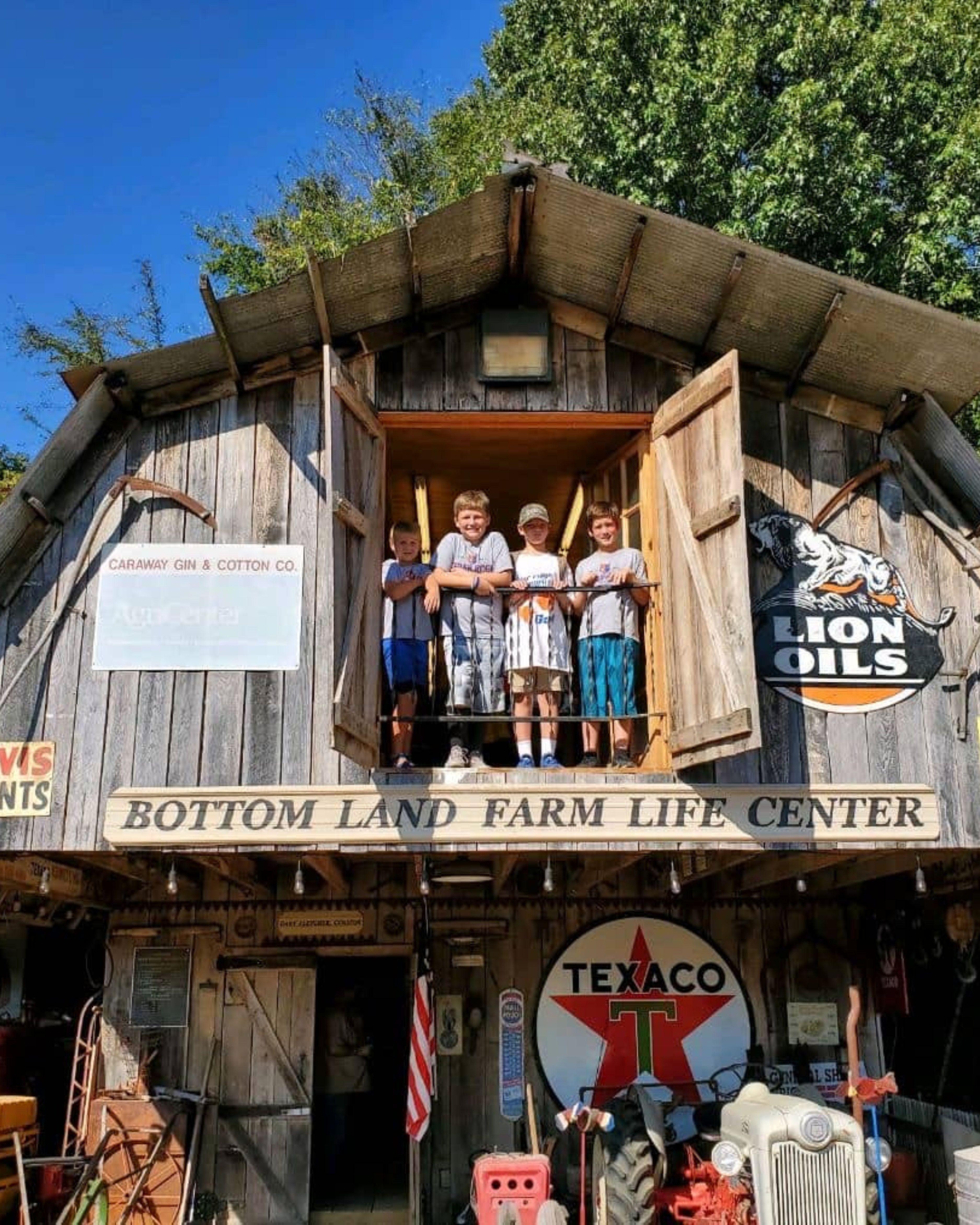 Bottom Land Farm Life Center in Fair Haven, NJ, featuring a rustic barn-style building with vintage farm memorabilia, antique signage, and children standing in the upper loft on a sunny day.