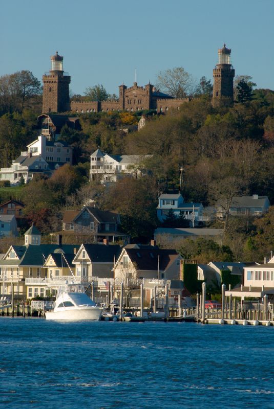 Waterfront view of Highlands, New Jersey, with marina docks, boats, coastal homes, and the historic Twin Lights of Navesink rising above the community.