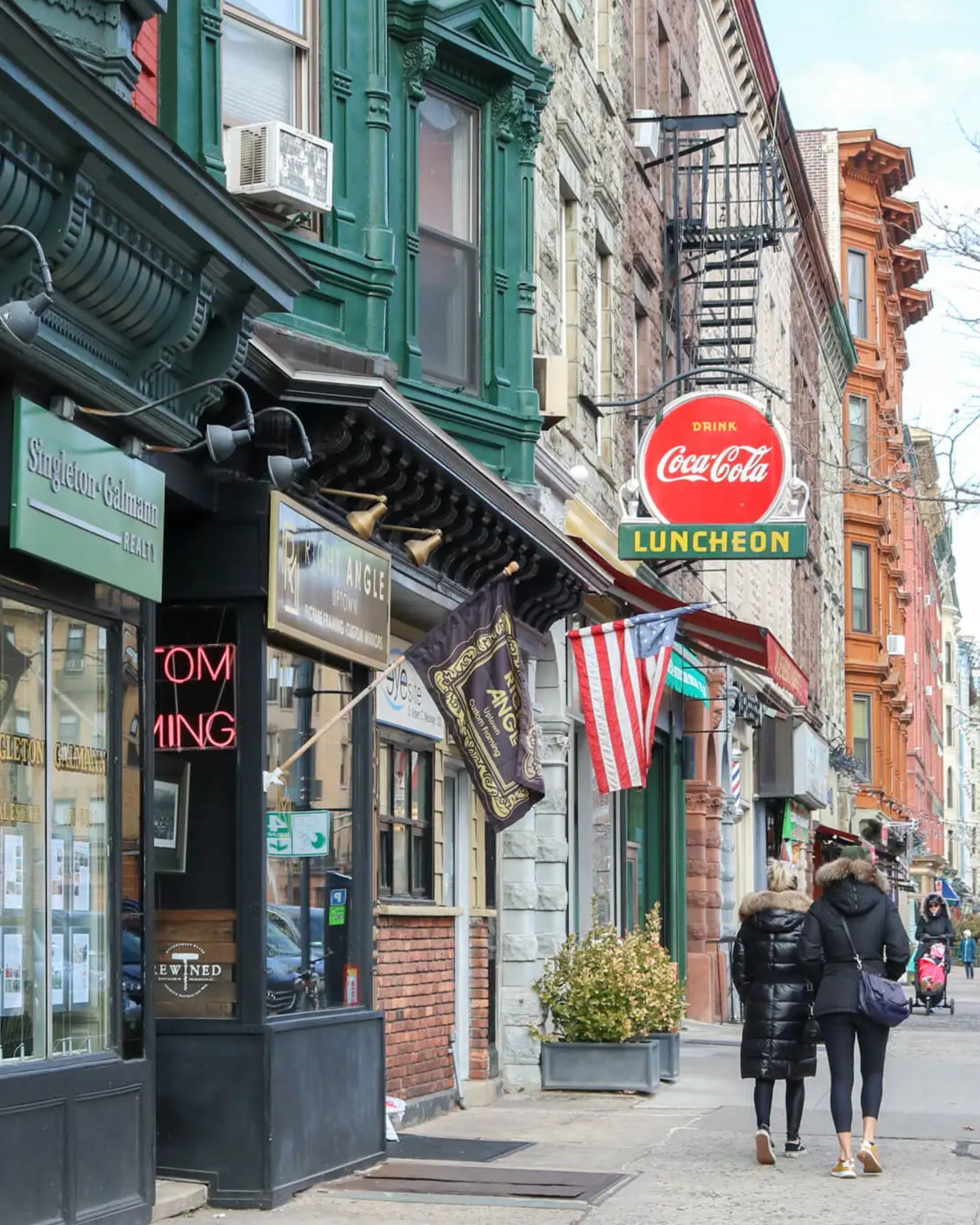 Historic street scene in Hoboken, New Jersey, featuring colorful storefronts, classic brownstone architecture, local shops, and pedestrians walking through the neighborhood.