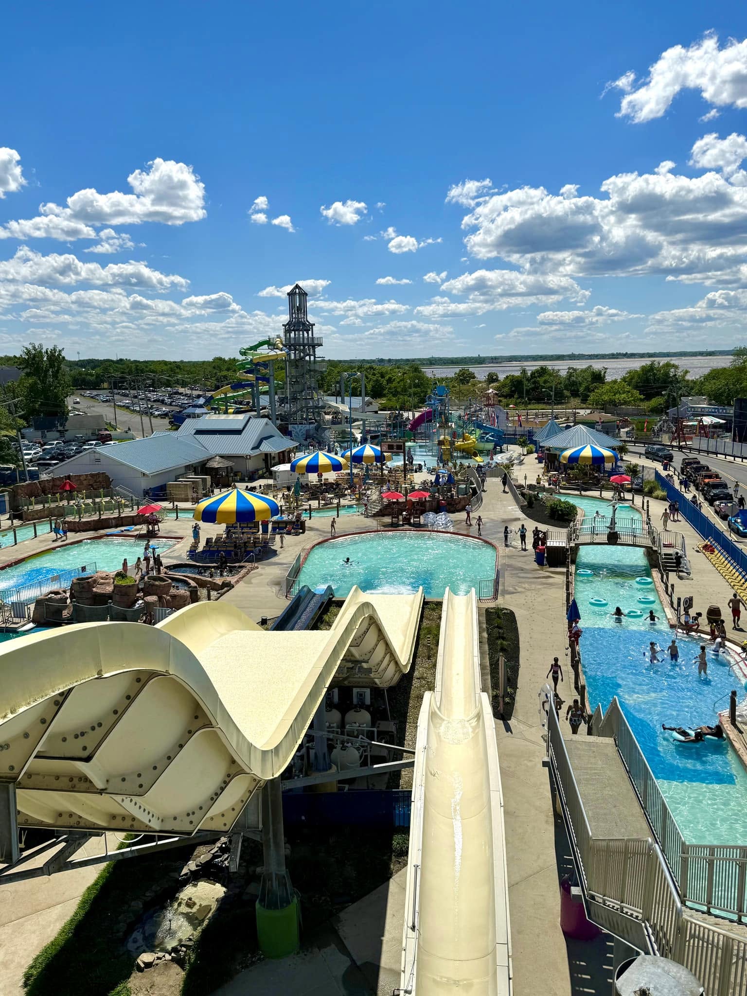 Water slides, pools, colorful umbrellas, and family attractions at a water park in Keansburg, New Jersey, with amusement park rides visible in the background.