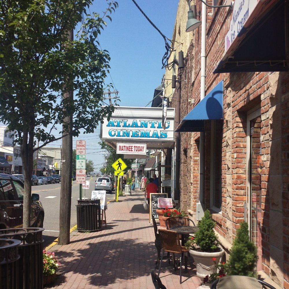 Atlantic Cinemas theater sign along a brick-lined downtown street near Leonardo, New Jersey, with local storefronts, sidewalk seating, and pedestrians.